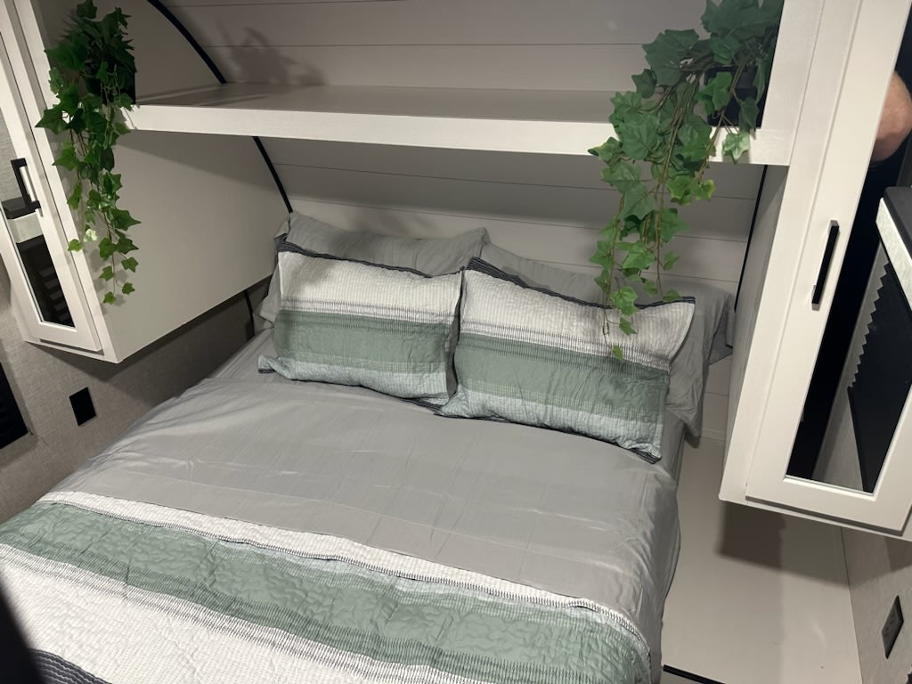 This inviting RV rental bedroom features a comfy bed with green accents, white overhead storage, and plant decor.. Jayco Jay Flight 2024