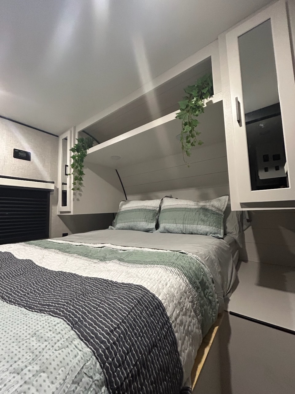 Cozy modern RV rental bedroom featuring a bed with striped bedding, overhead shelves with hanging plants, and white cabinetry.. Jayco Jay Flight 2024