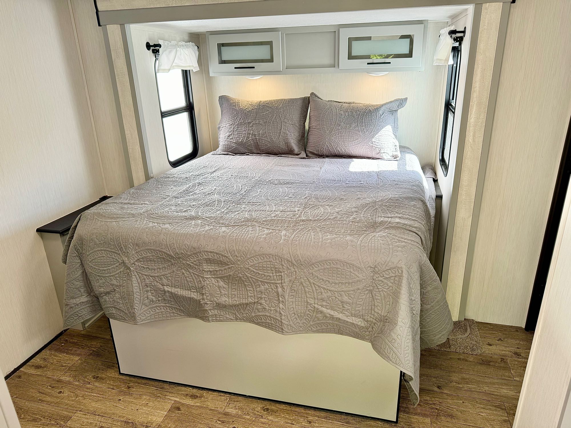 This inviting RV rental bedroom features a large bed with quilted linens, overhead cabinets, and dual windows.. Forest River Vibe 2021
