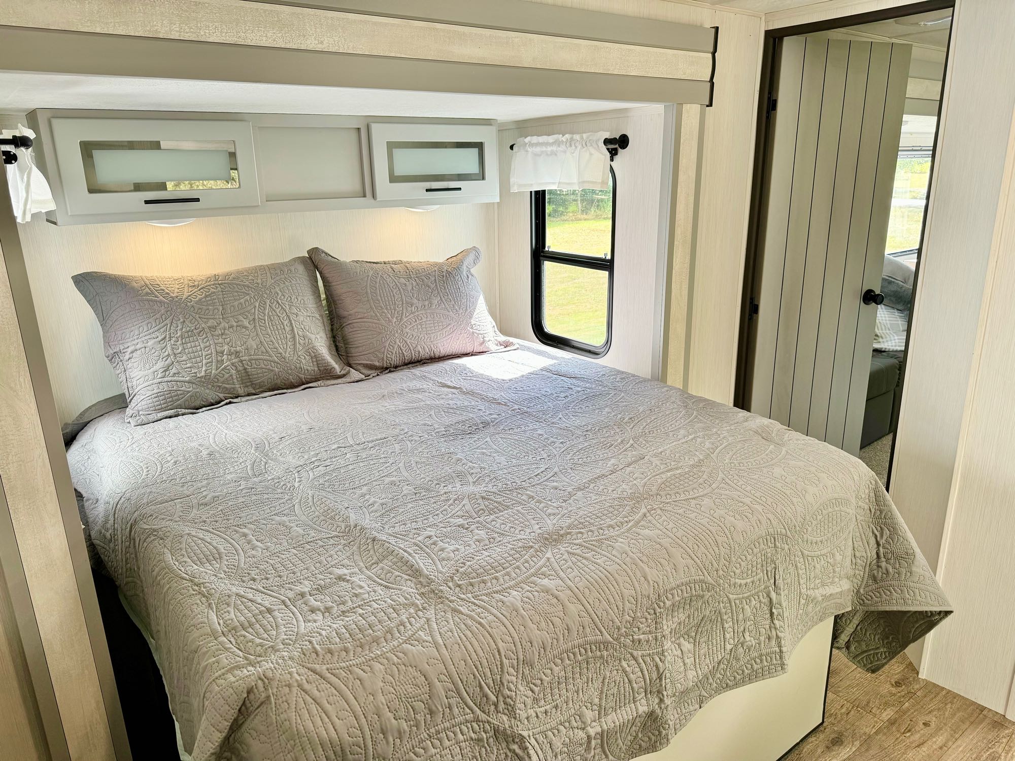 Modern RV rental bedroom featuring a comfy bed, overhead cabinets, and a scenic window. Ideal for travel.. Forest River Vibe 2021
