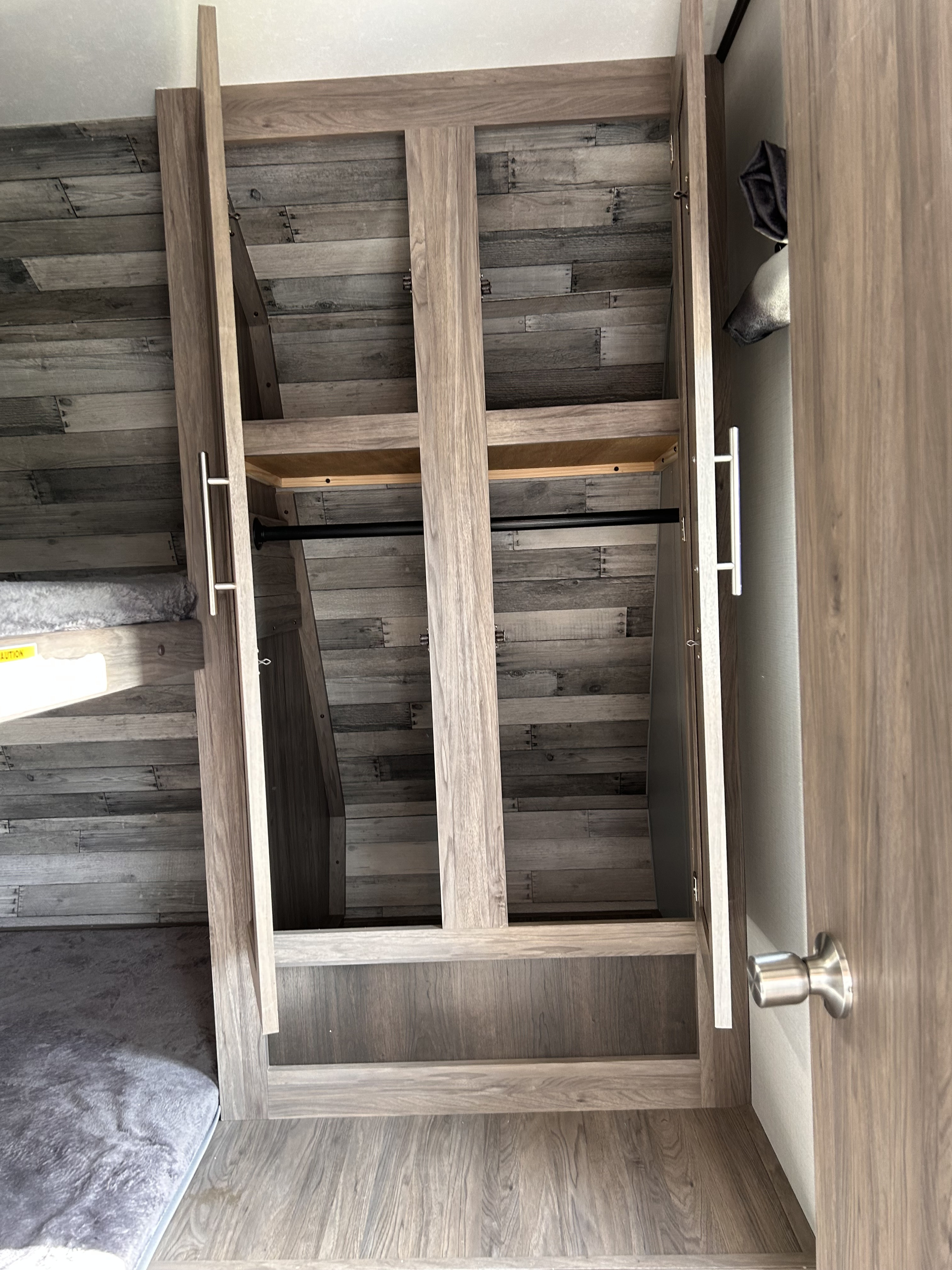 RV rental interior: cozy bunk bed and open wardrobe featuring a hanging rod and shelf, with modern wood finishes.. Crossroads RV Zinger 2021