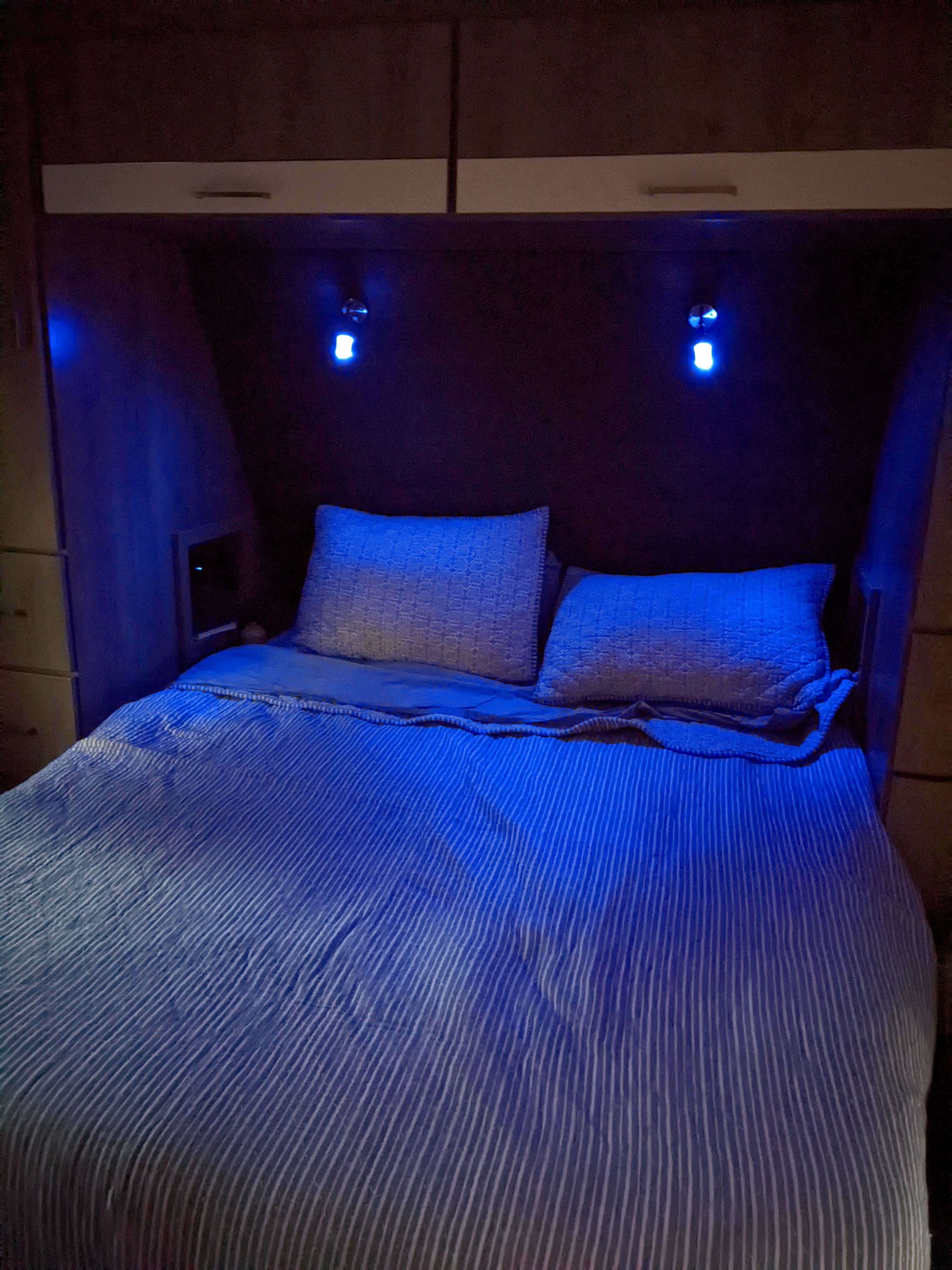 Comfortable RV rental bedroom with a striped bed and atmospheric blue lighting.. Grand Design Imagine 2022
