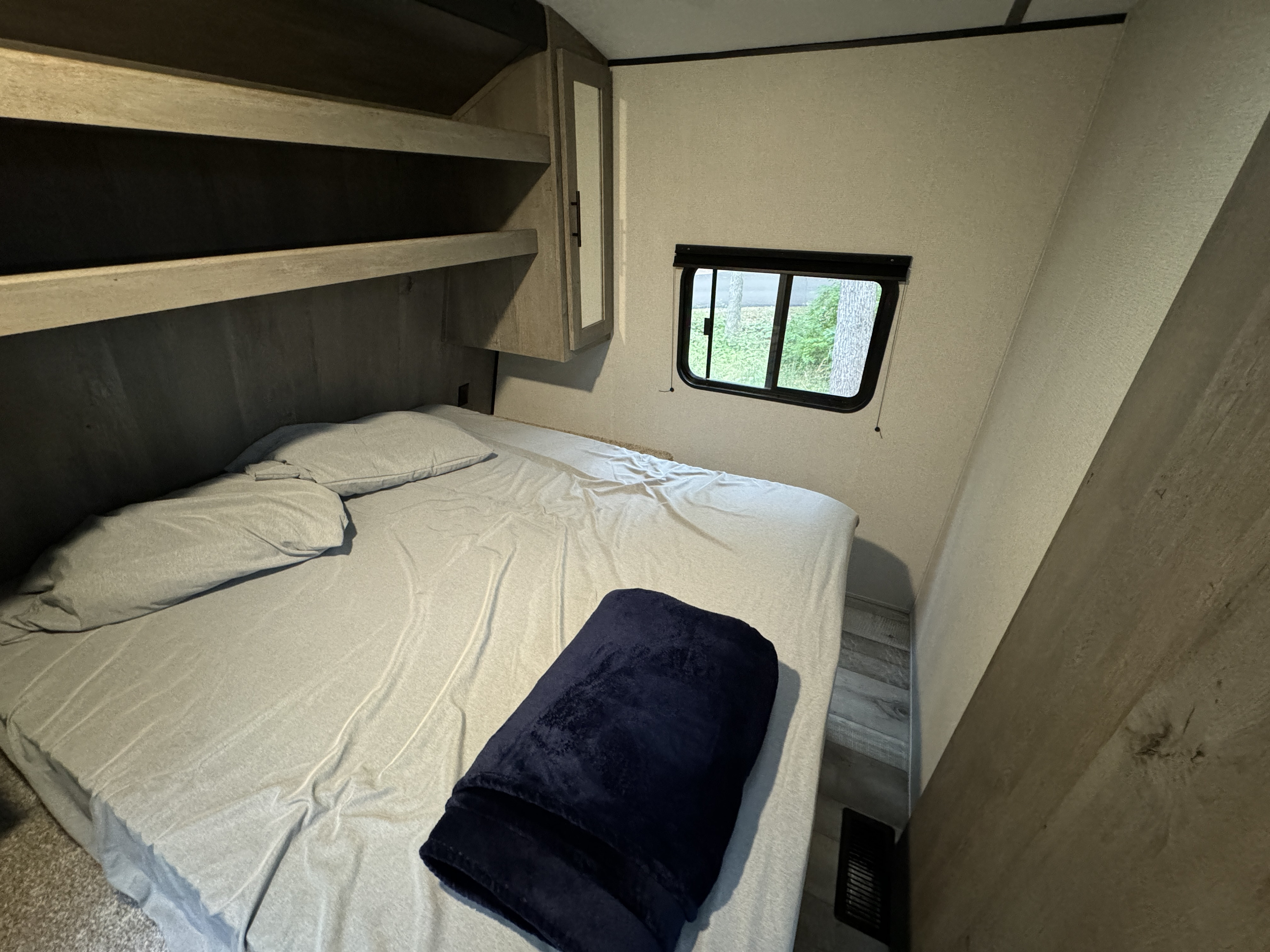 Cozy RV rental bedroom featuring a comfy bed, overhead storage, and a window with a view. Ideal for your next adventure.. Keystone Springdale 2021