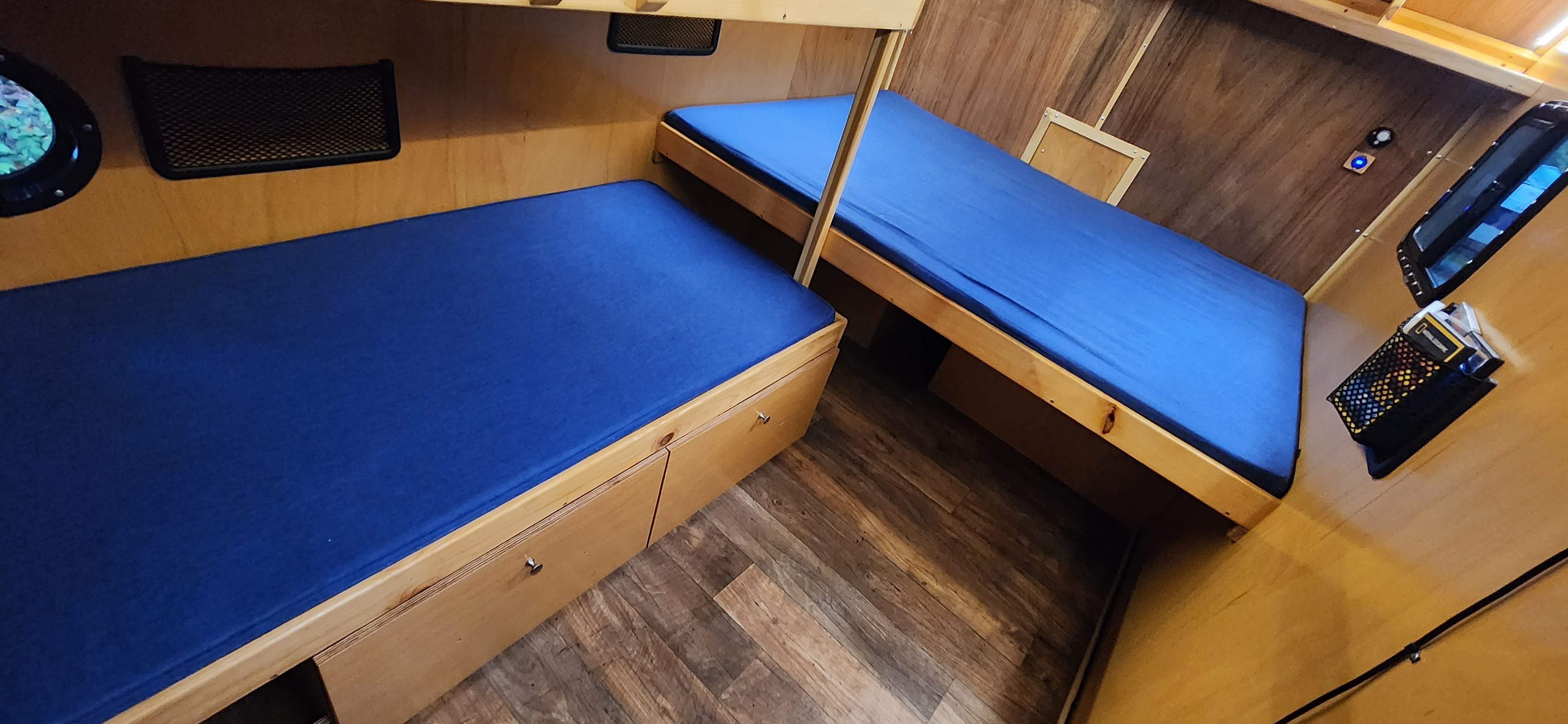 Cozy RV rental interior with two compact bunk beds featuring blue mattresses, wooden paneling, and built-in storage.. Bend Teardrop Tall Boy 2023