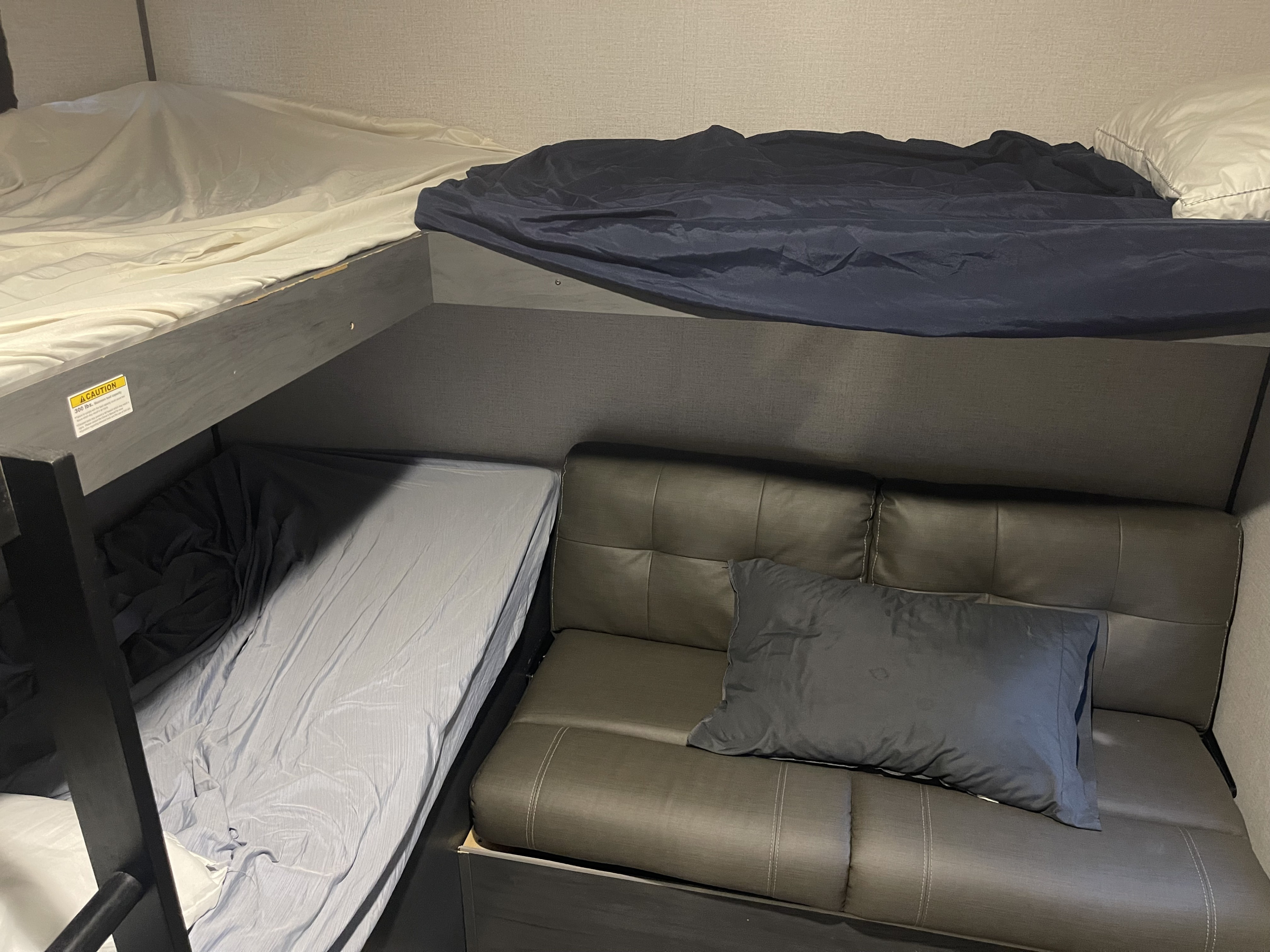 RV rental interior featuring a two-tier bunk bed with bedding & a sofa with a cushion, ideal for compact travel accommodations.. Dutchmen Aspen Trail 2021