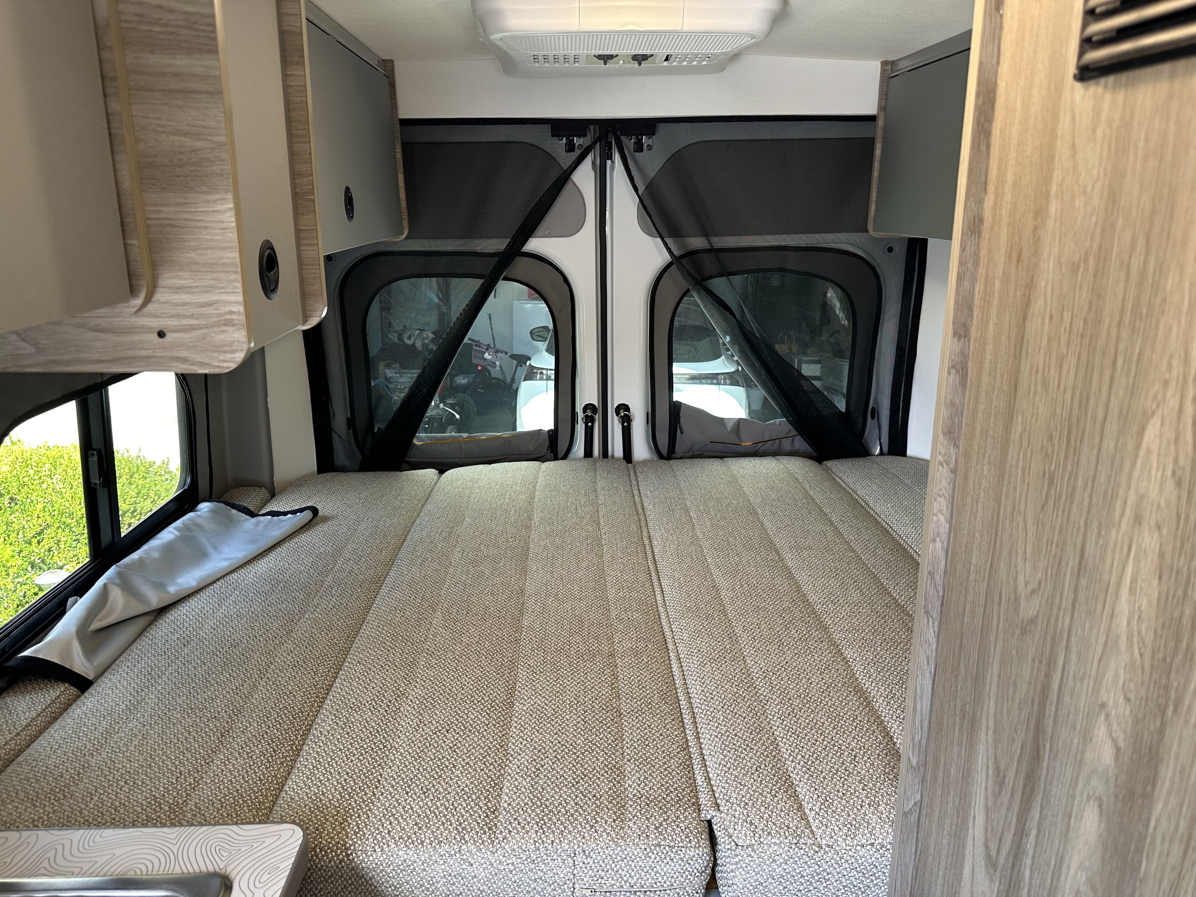 Inside this RV rental, a comfy modular bed fills the rear, with screened doors offering outdoor views.. Winnebago Solis 2025