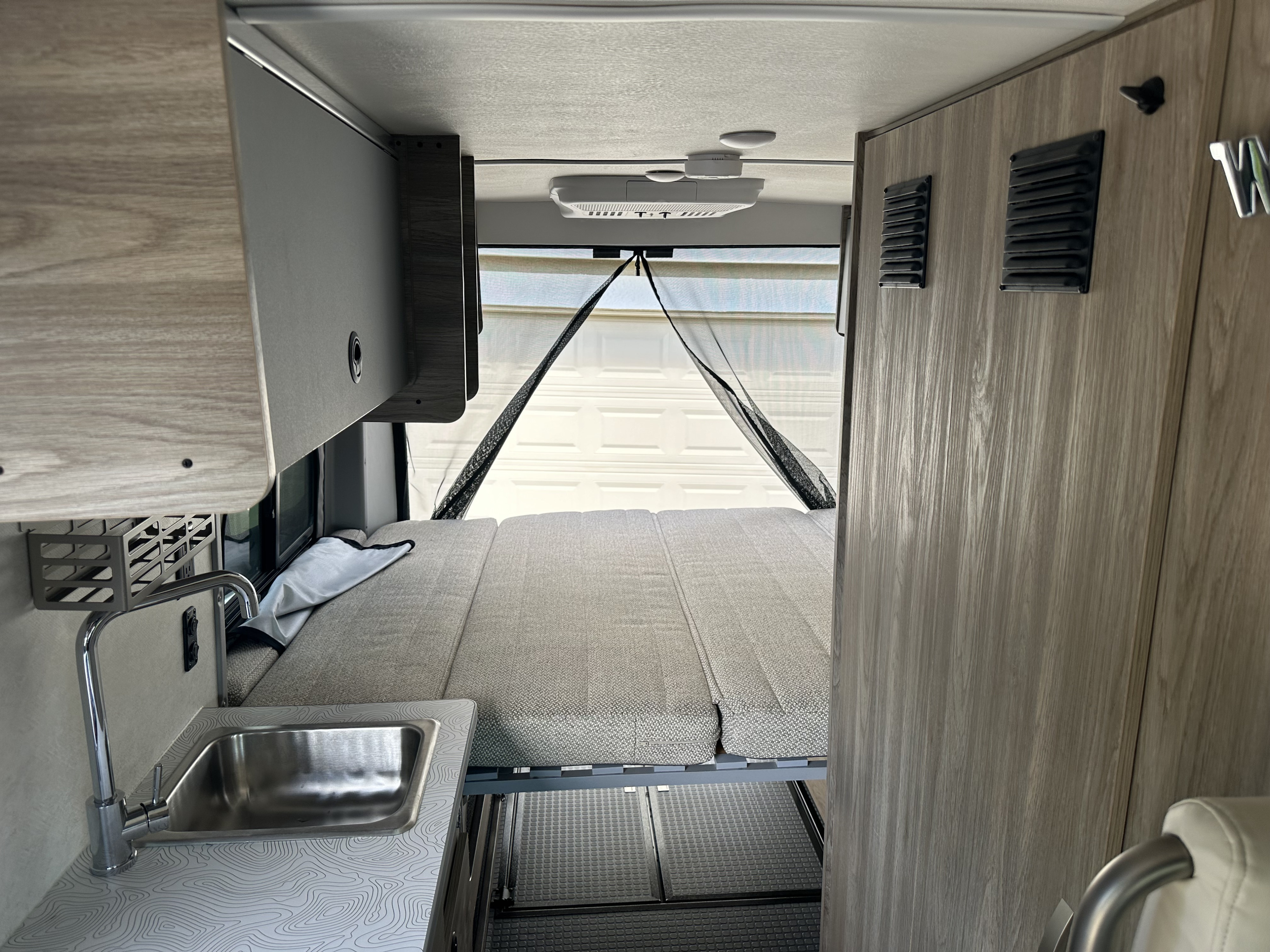RV rental interior featuring a convertible bed, compact kitchen with sink, and overhead storage. Ideal for travel.. Winnebago Solis 2025