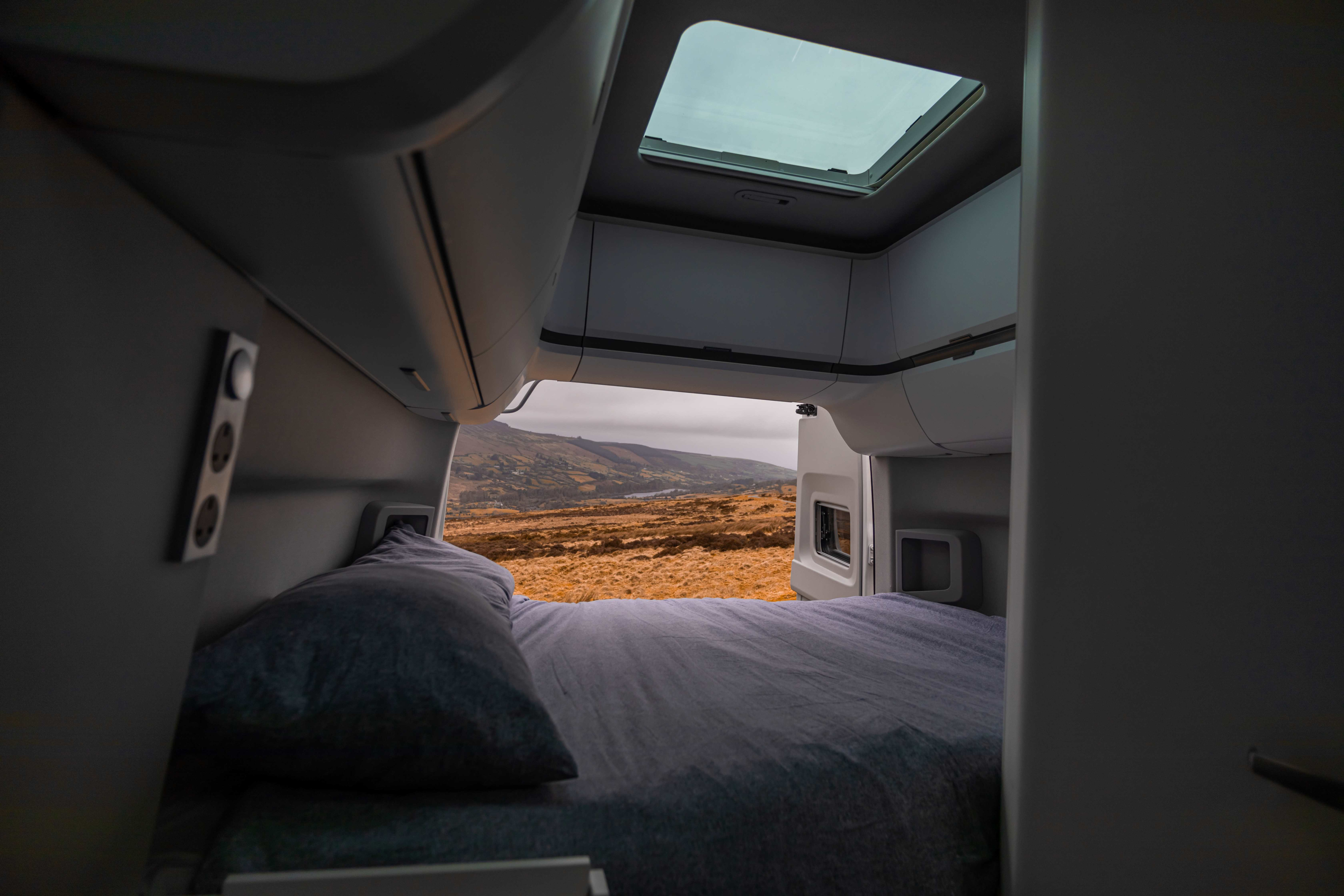 Experience nature with an RV rental: Cozy bed view of rolling golden hills & distant lake from inside a modern camper.. Volkswagen Grand California 2024