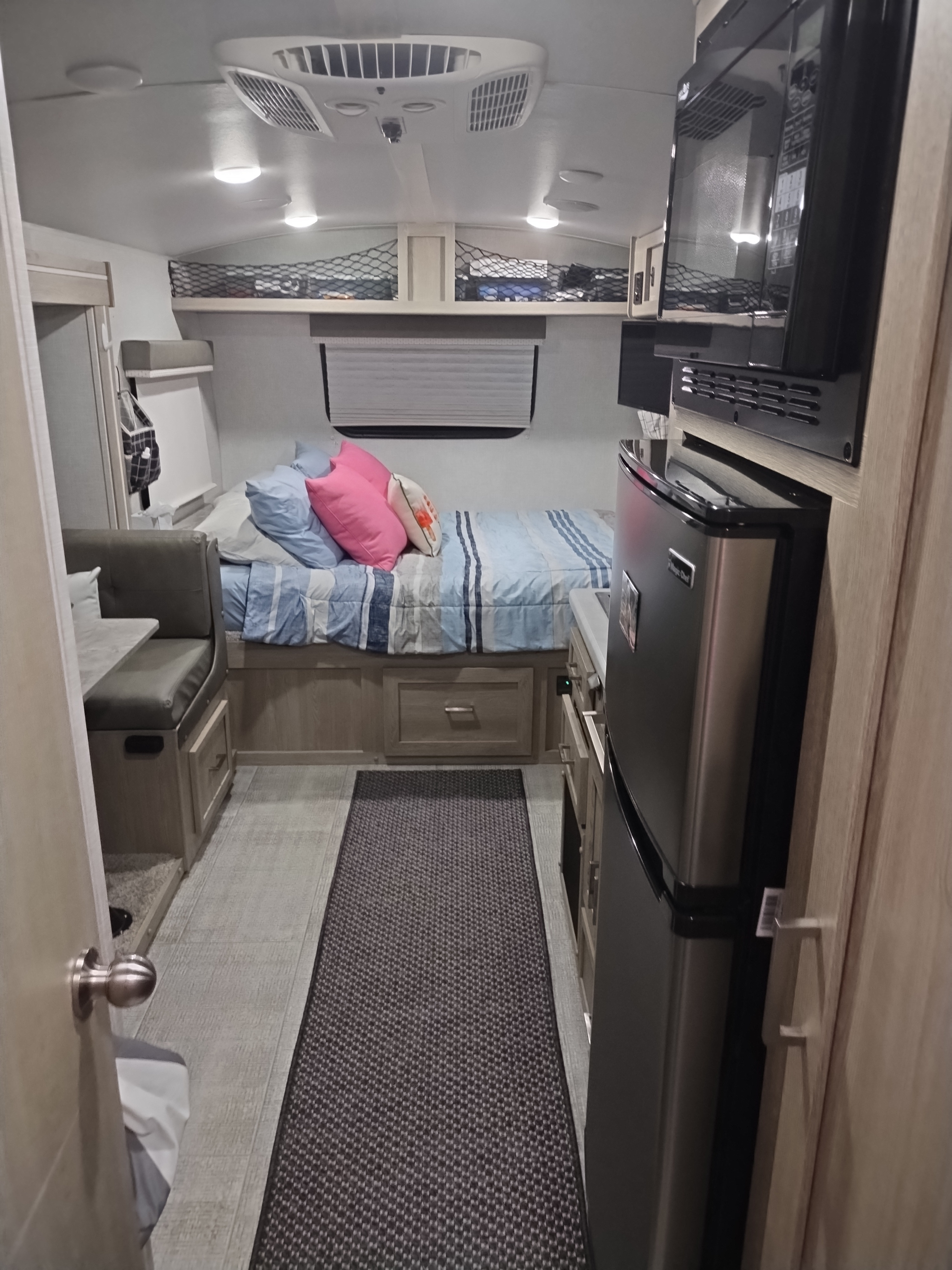 Compact RV rental interior featuring a cozy bed, dinette, and a functional kitchen with microwave and fridge.. Forest River Rockwood Geo Pro 2021
