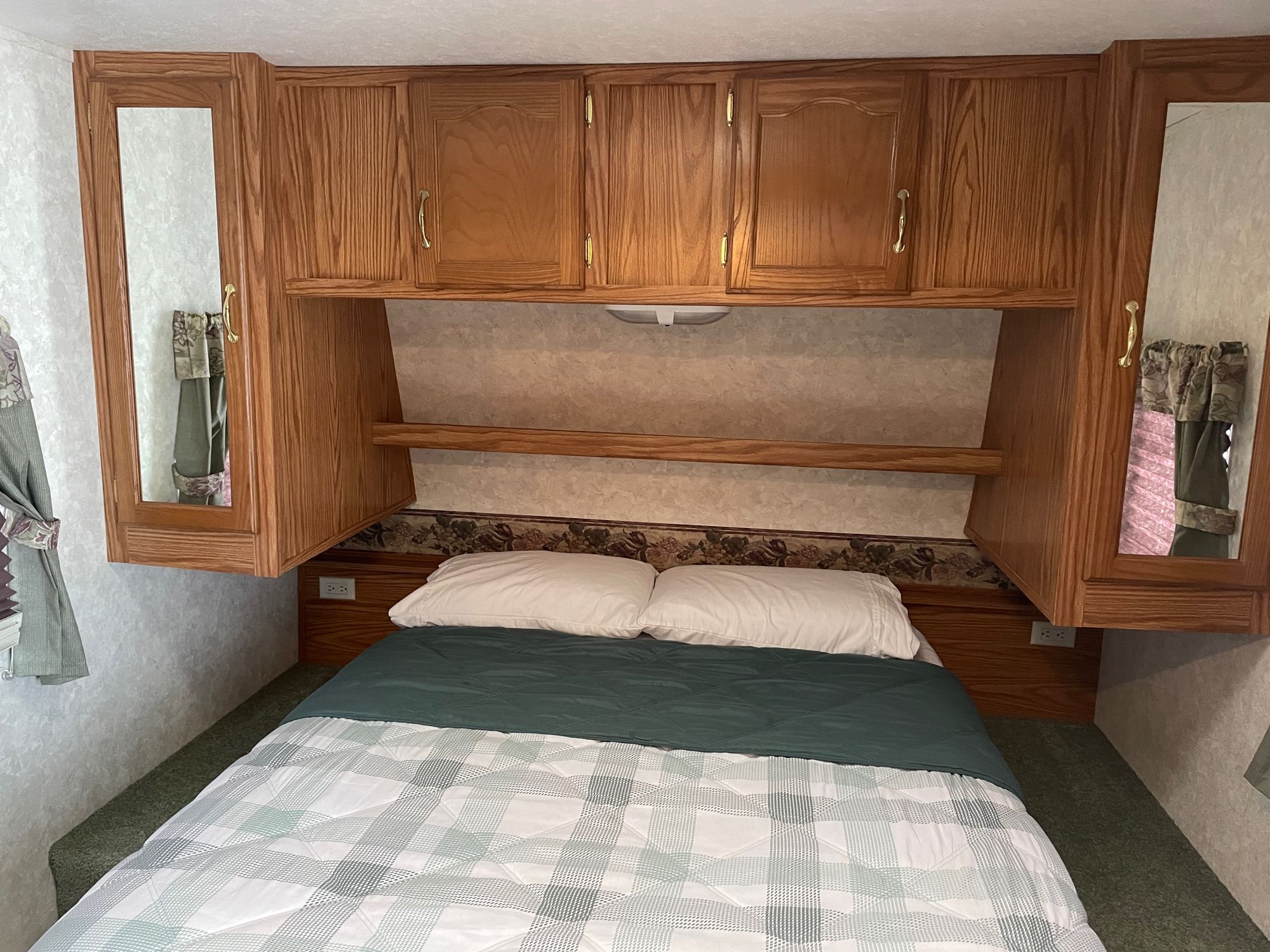 RV rental bedroom featuring wood overhead cabinets, mirrored doors, and a cozy plaid bed.. Keystone RV Cougar 2003