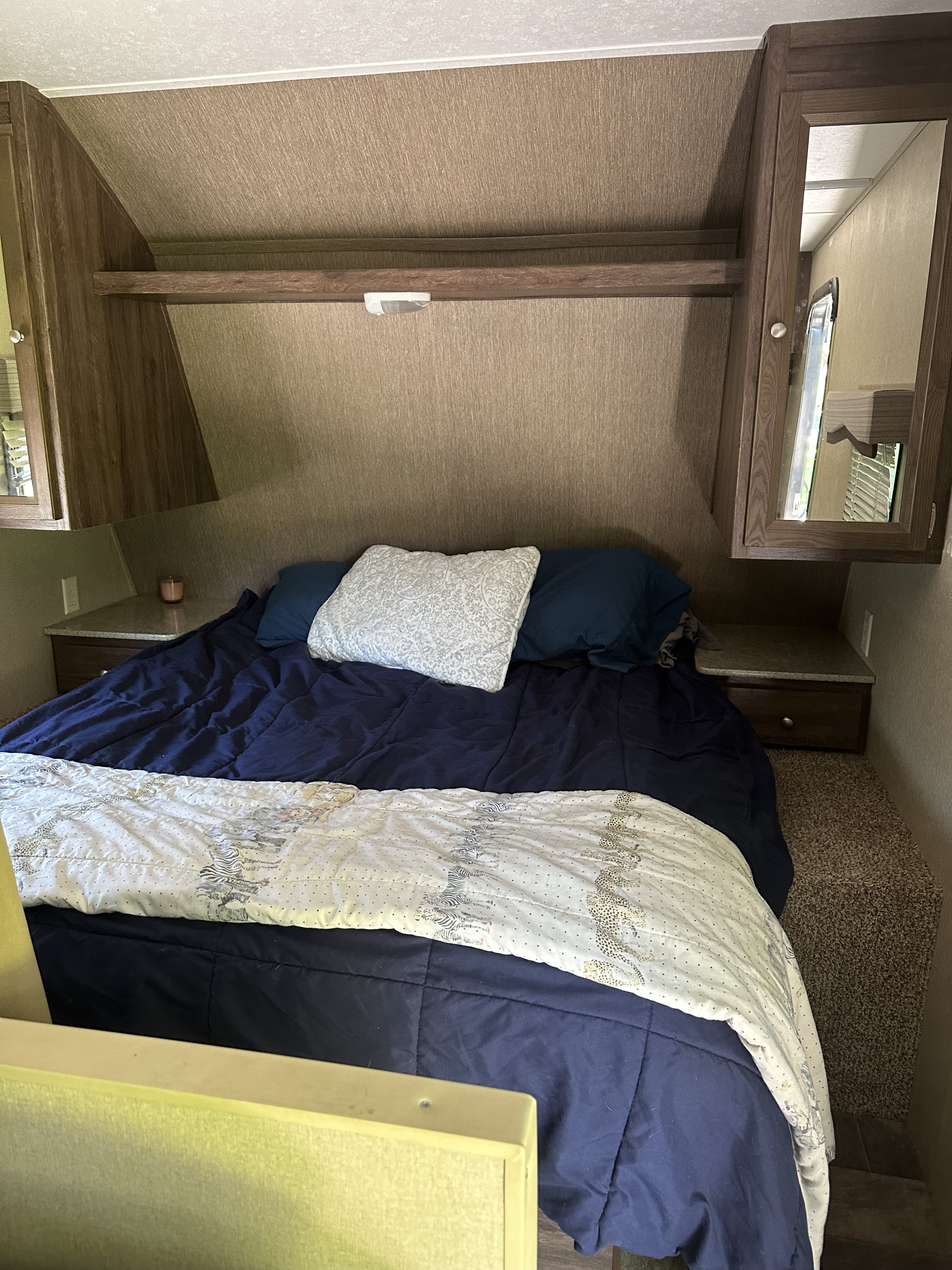 Cozy RV rental bedroom with dark blue bedding, overhead cabinets, and built-in nightstands for a comfortable stay.. Dutchmen Coleman Lantern 2015