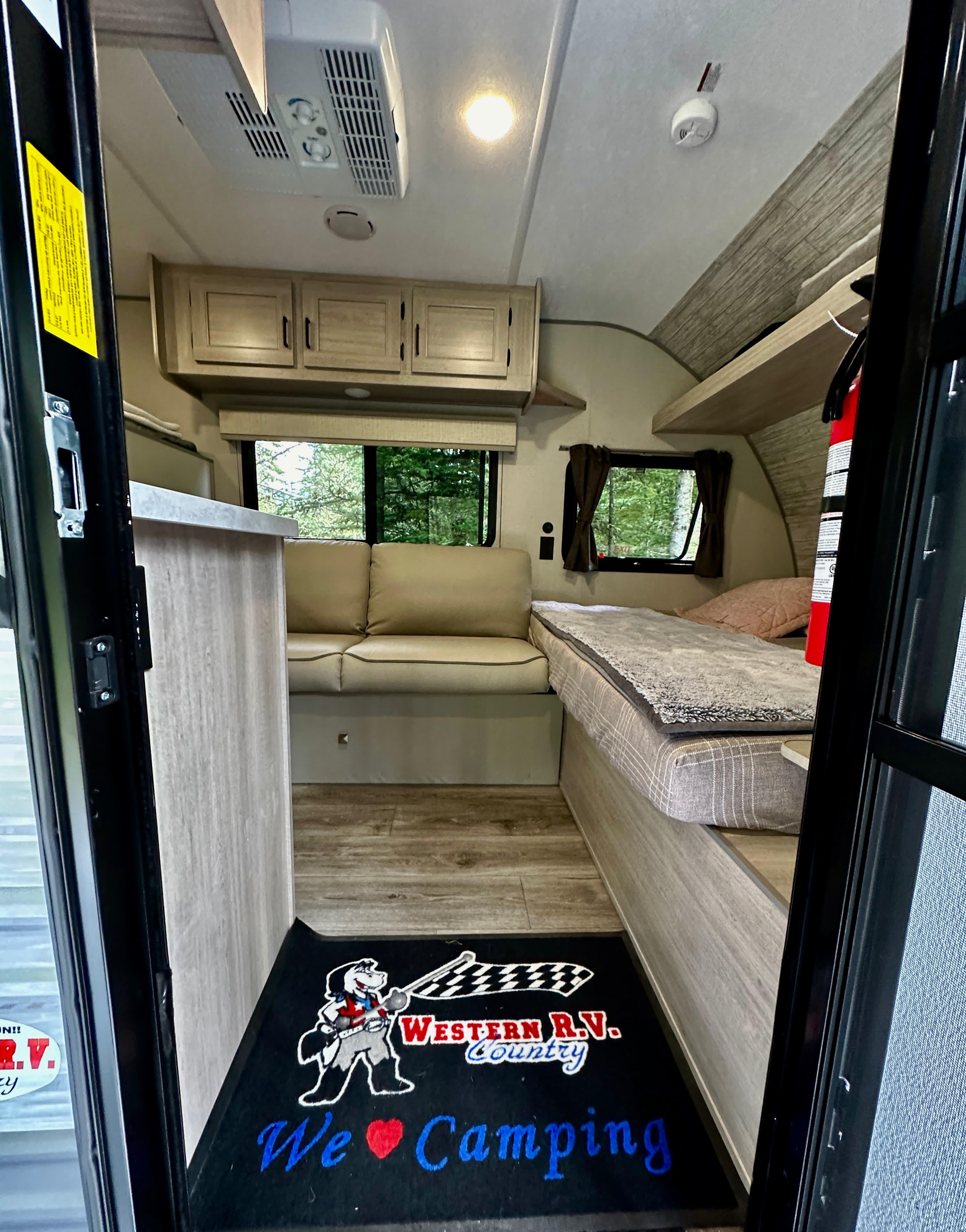 Step inside this inviting rv rental interior, showcasing a bed, sofa, kitchen area, and a "We ❤️ Camping" mat at the entrance.. Coachmen 164 BHX 2024