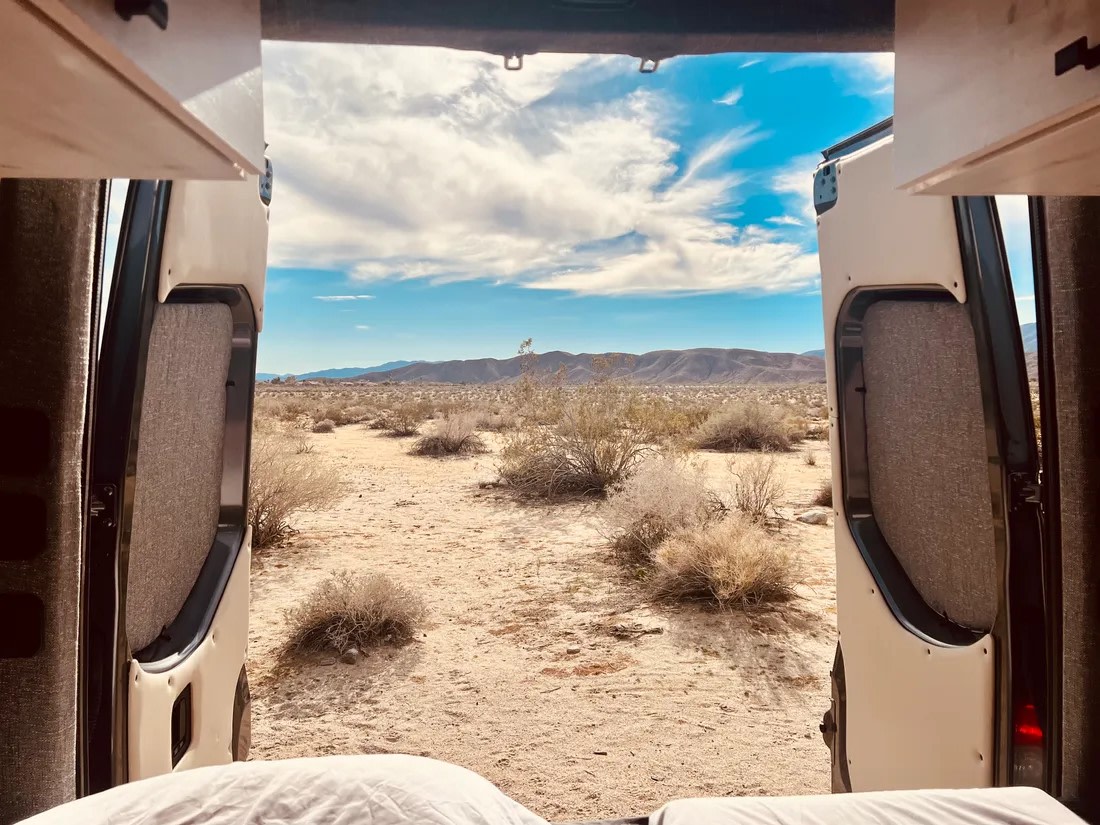 Enjoy desert views from your RV rental. Open van doors reveal a vast, scrubby landscape & distant mountains under a blue sky.. Sandy Vans Sprinter 2022
