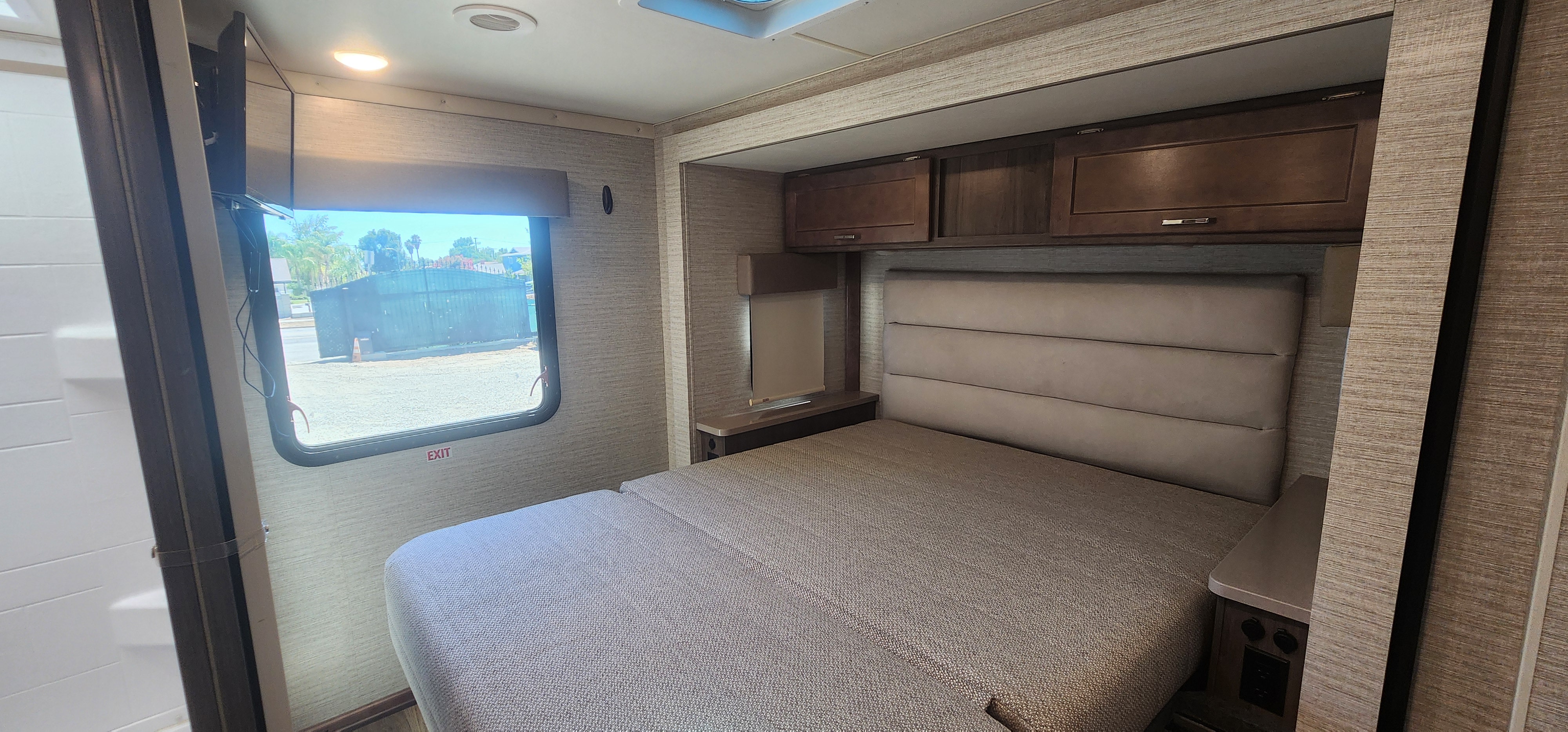 RV rental interior: a clean bedroom with a comfortable bed, padded headboard, overhead cabinets, TV, and an exit window.. Winnebago Minnie Winnie 2022