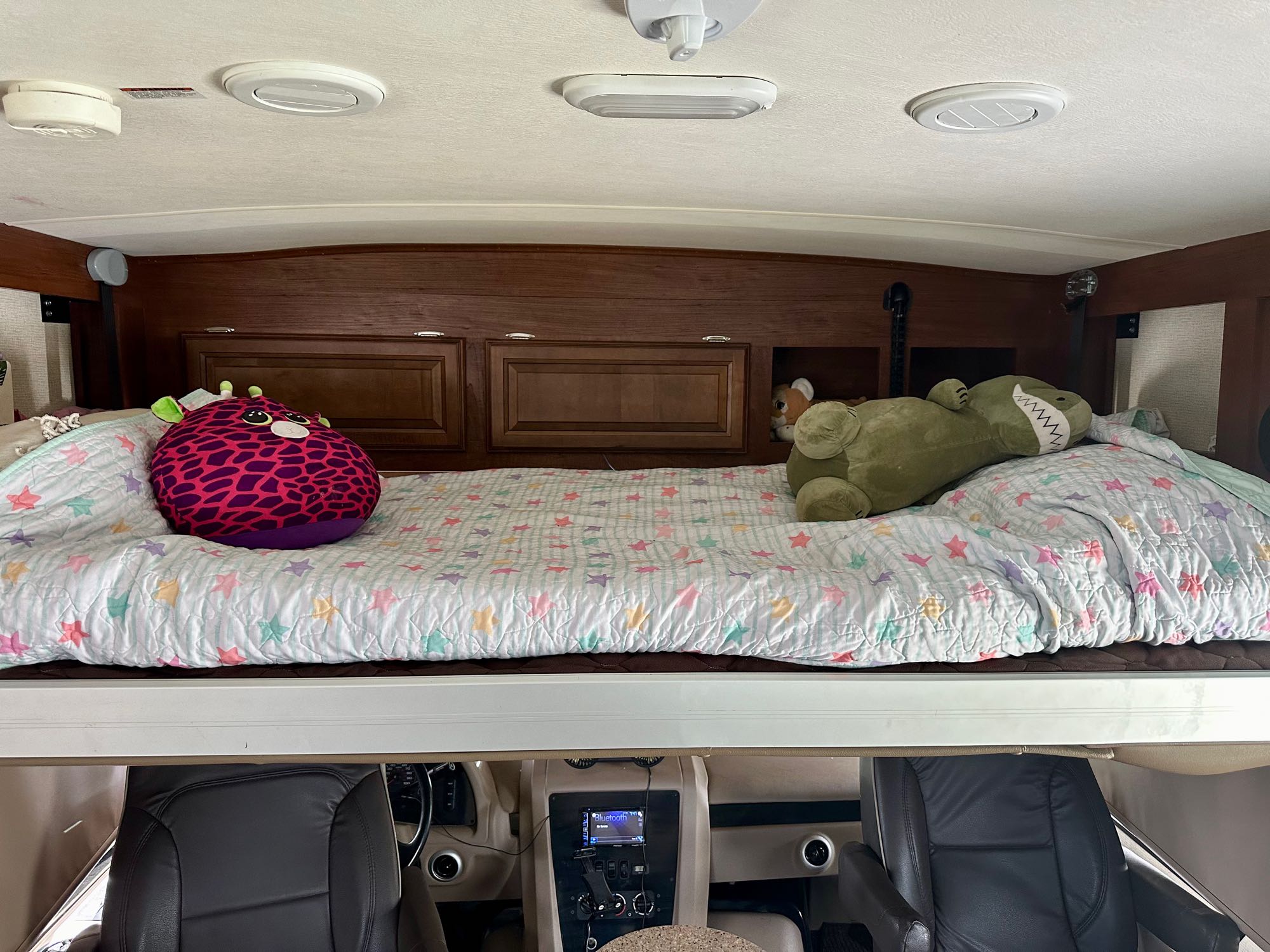 This cozy RV rental features an overhead bunk with a star-patterned quilt and two stuffed animals, overlooking the driver's cab.. Georgetown GT3 2017