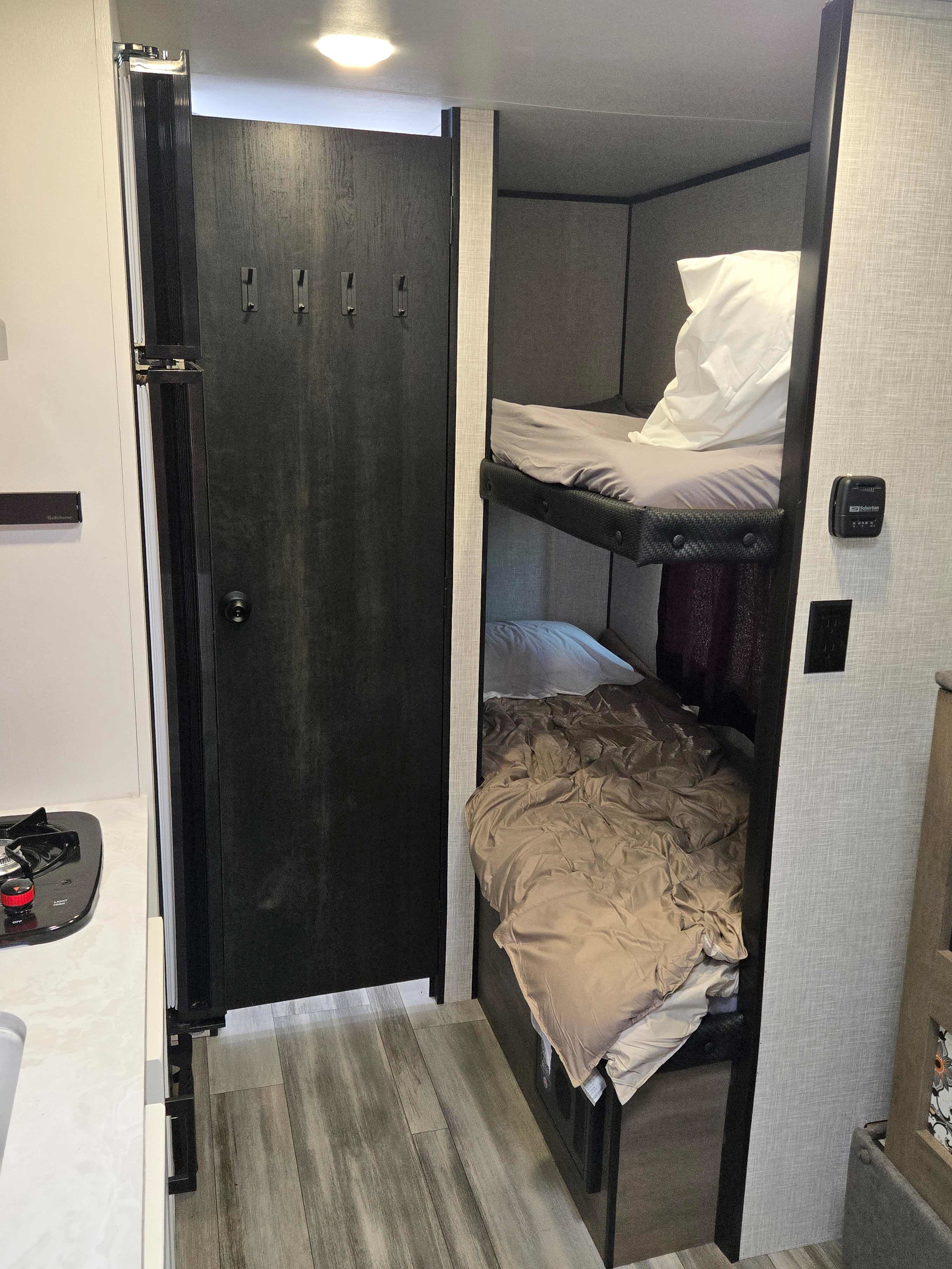 This RV rental interior features cozy bunk beds, a compact kitchen with a stove, and a space-saving folding door. Great for adventures!. Jayco Jay Flight SLX 2024