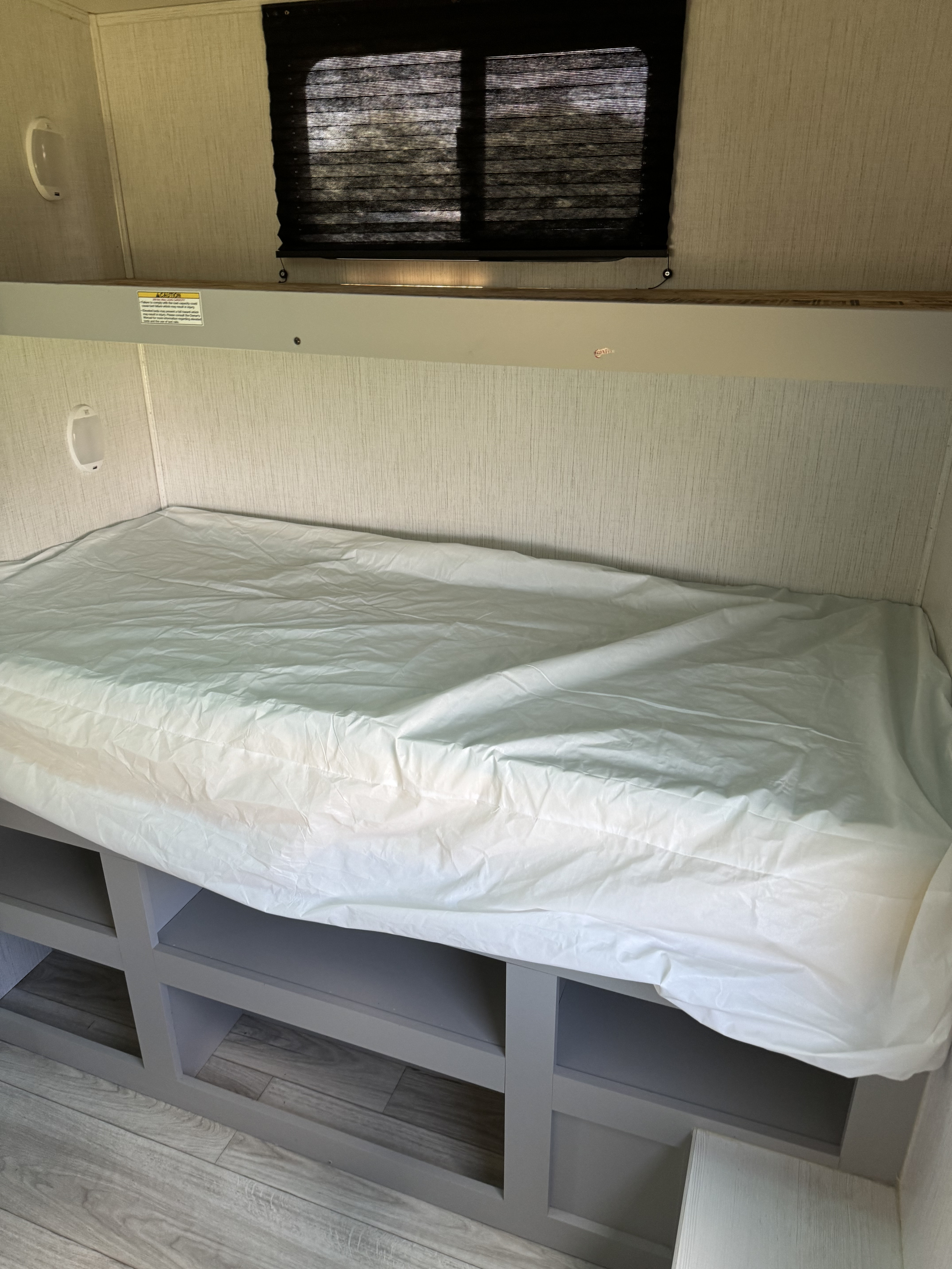 This RV rental features a cozy bunk bed with storage shelves below, a window with blinds, and an interior light.. Heartland RVs North Trail 2022