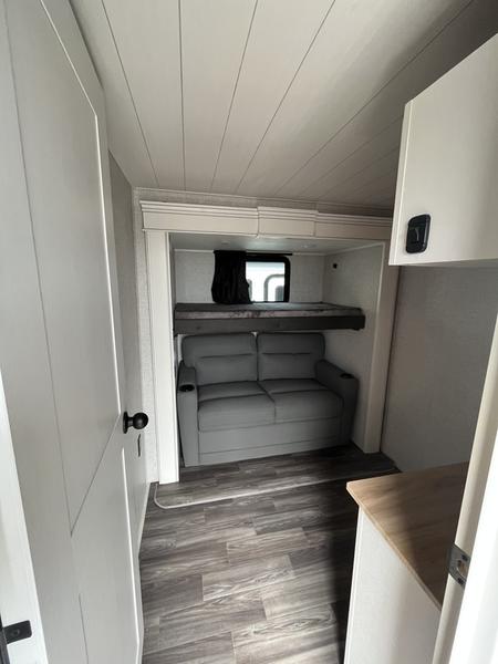 This RV rental's modern interior features a comfortable grey sofa below a bunk bed setup with a window, all on wood-look flooring.. Jayco Eagle 2024