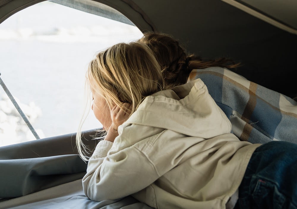 Child and adult relaxing in their RV rental, enjoying the window view.. Winnebago Solis 2023
