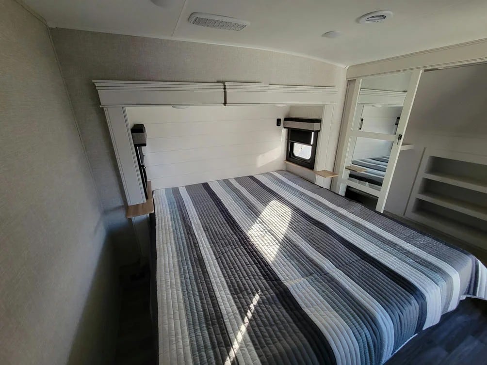Experience comfort in this RV rental bedroom. Features a cozy bed, window, and mirrored closet with built-in ladder & shelves.. Jayco Eagle 2024