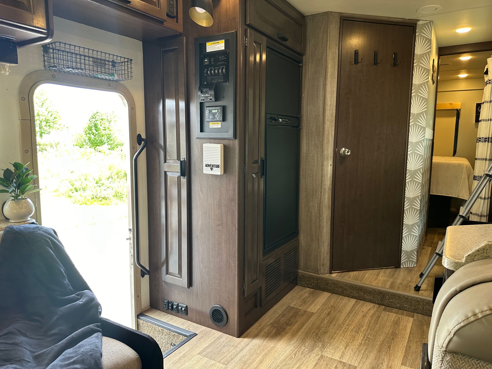 RV rental interior: control panel, fridge, and door open to nature. Cozy seating and bedroom visible.. Thor Four Winds 2017