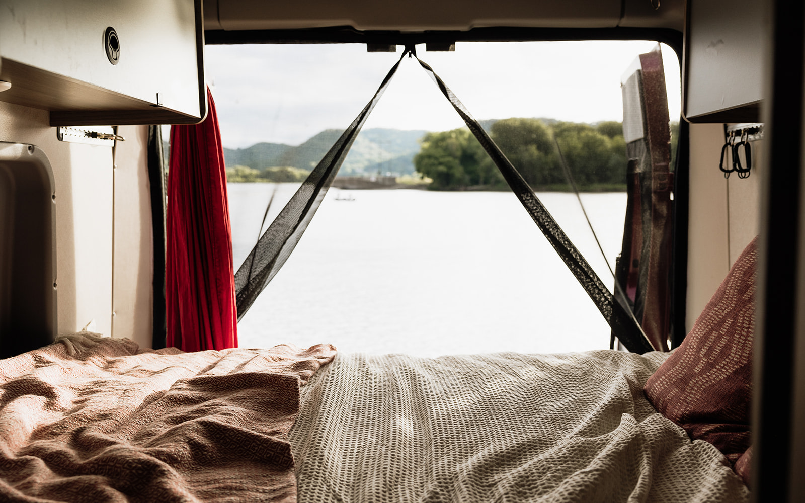 Inside an RV rental, a comfortable bed offers a relaxing view of a calm lake or river, complete with mosquito netting.. Winnebago Solis 2023