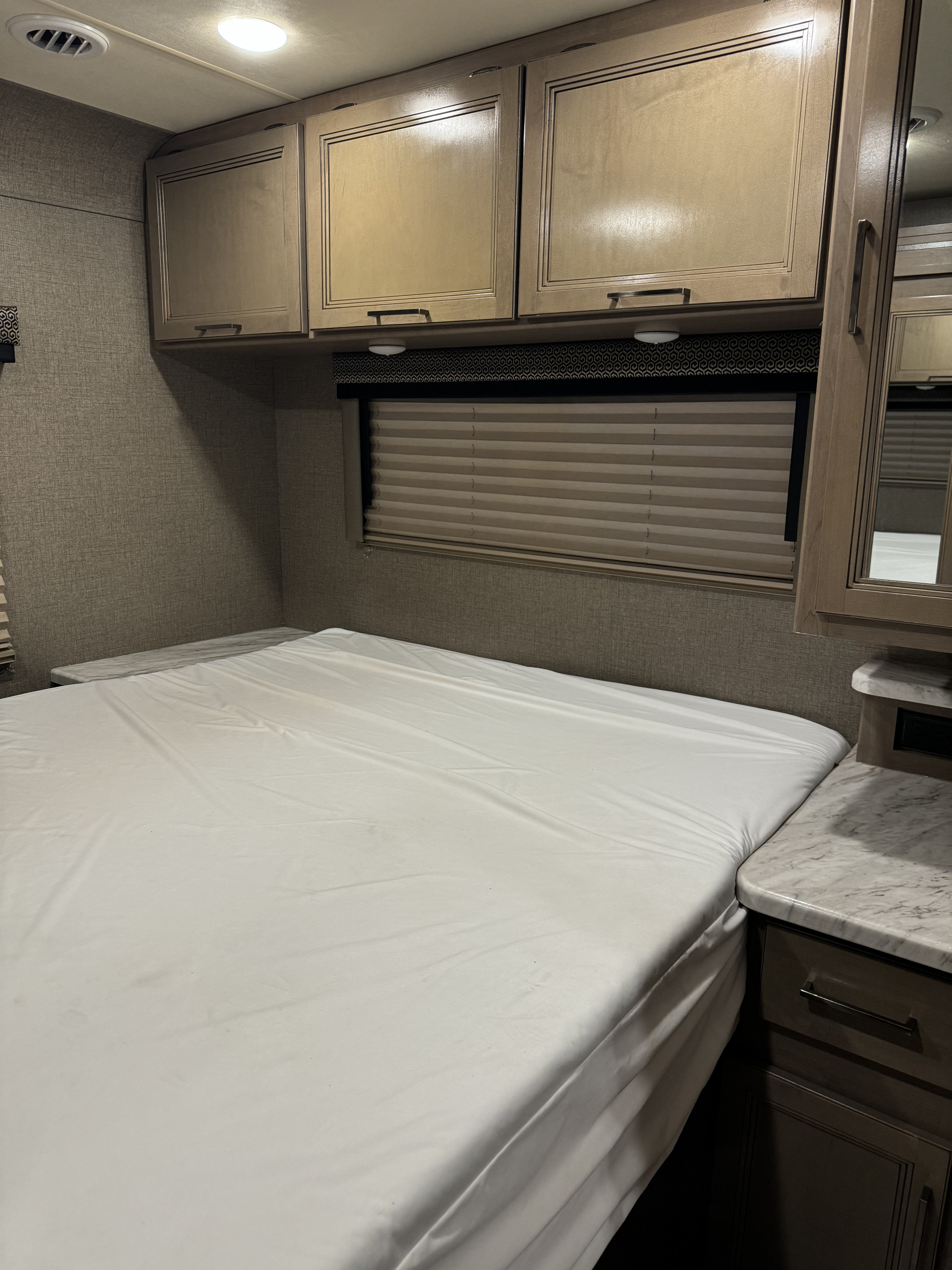 Cozy RV rental bedroom with clean bed, overhead cabinets, and window blinds. Ideal for travel.. Thor Coleman 2021