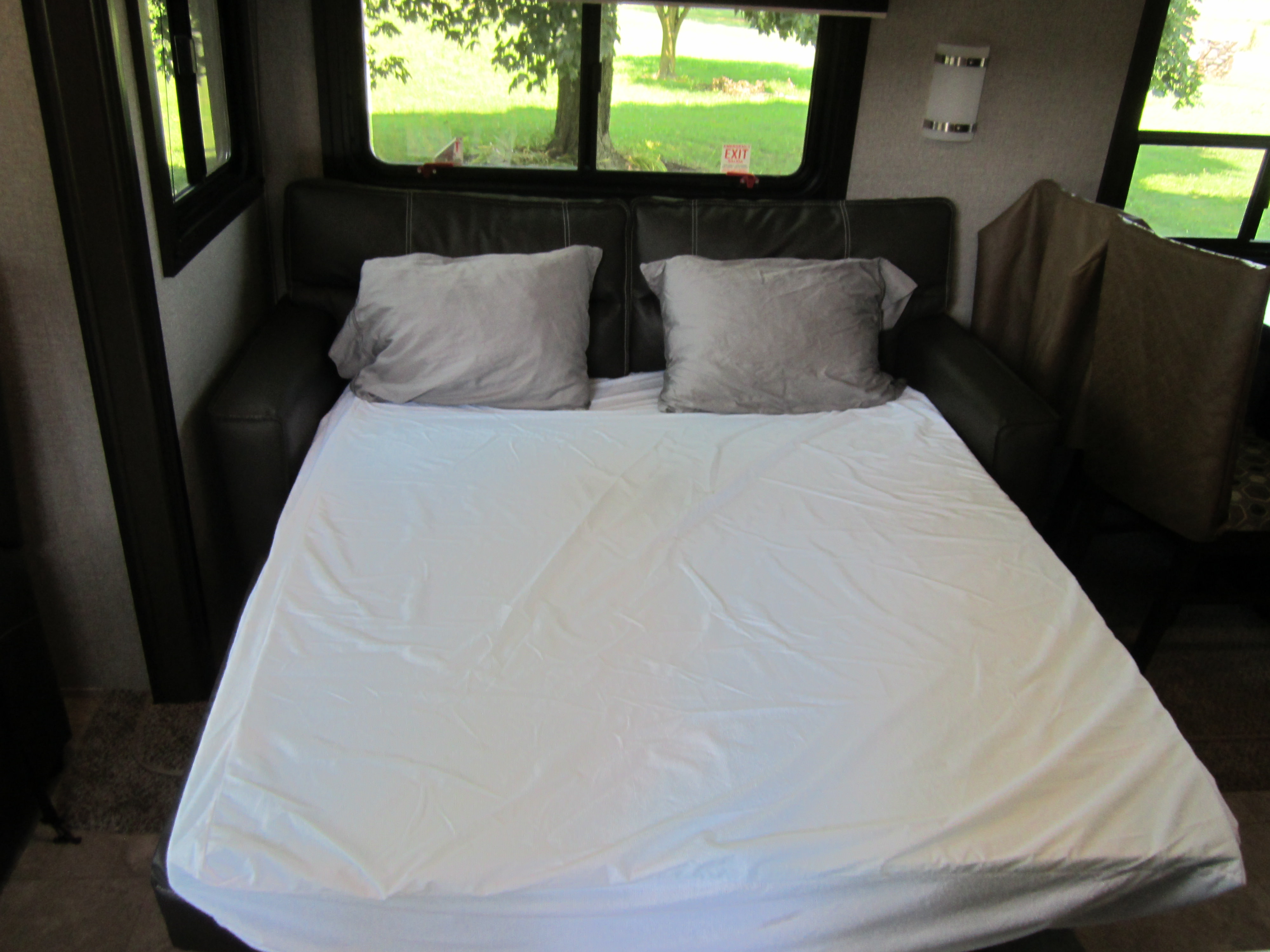This RV rental offers a comfy pull-out sofa bed with white sheets and pillows, overlooking a green landscape.. Jayco Jay Flight 2020