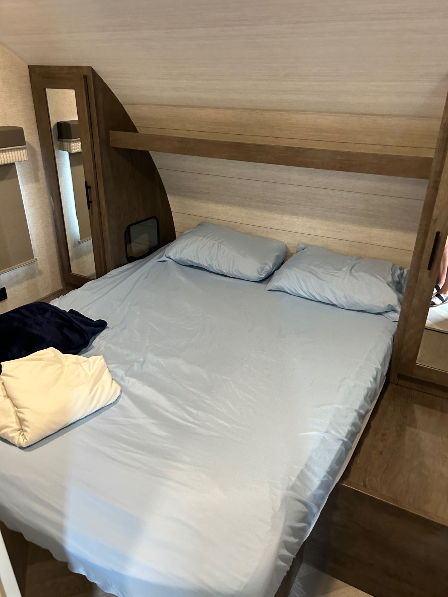 An RV rental bedroom with a bed, light blue sheets & pillows, and wooden built-in cabinets on each side.. Forest River Wildwood X-Lite 2021