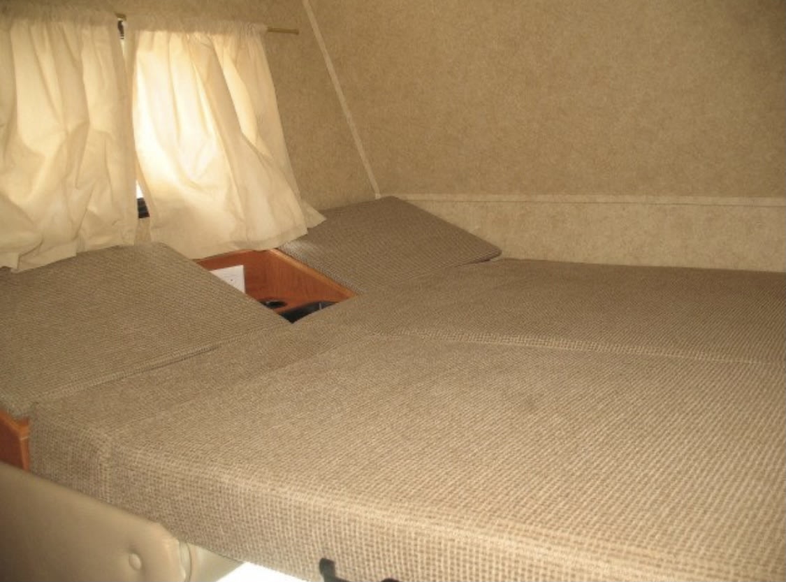 RV rental interior: A compact sleeping area with tan modular cushions forming a bed, featuring a central cutout and privacy curtains.. Forester Forester Motorhome 2012