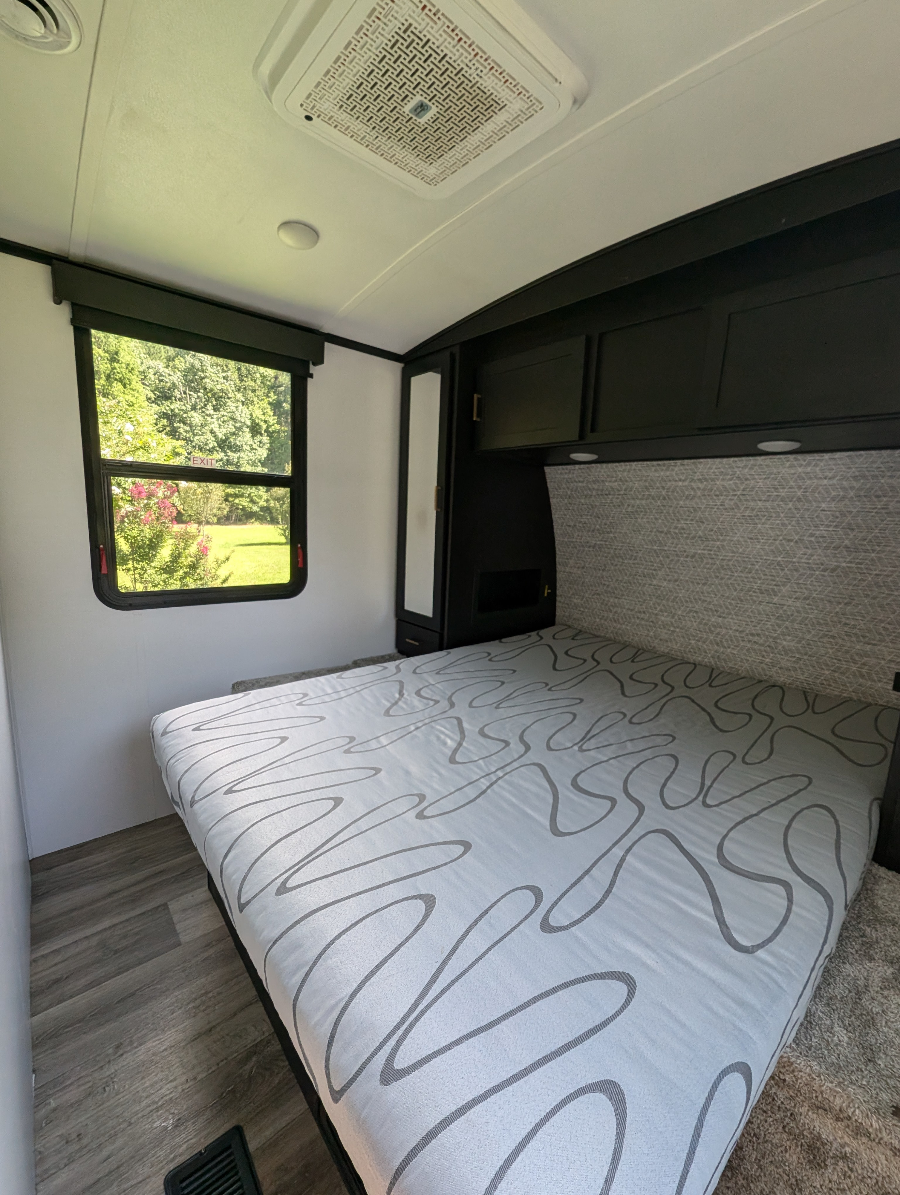 Cozy RV rental bedroom featuring a patterned bed, modern black cabinets, and a bright window with green outdoor views.. Keystone RV Outback 2022