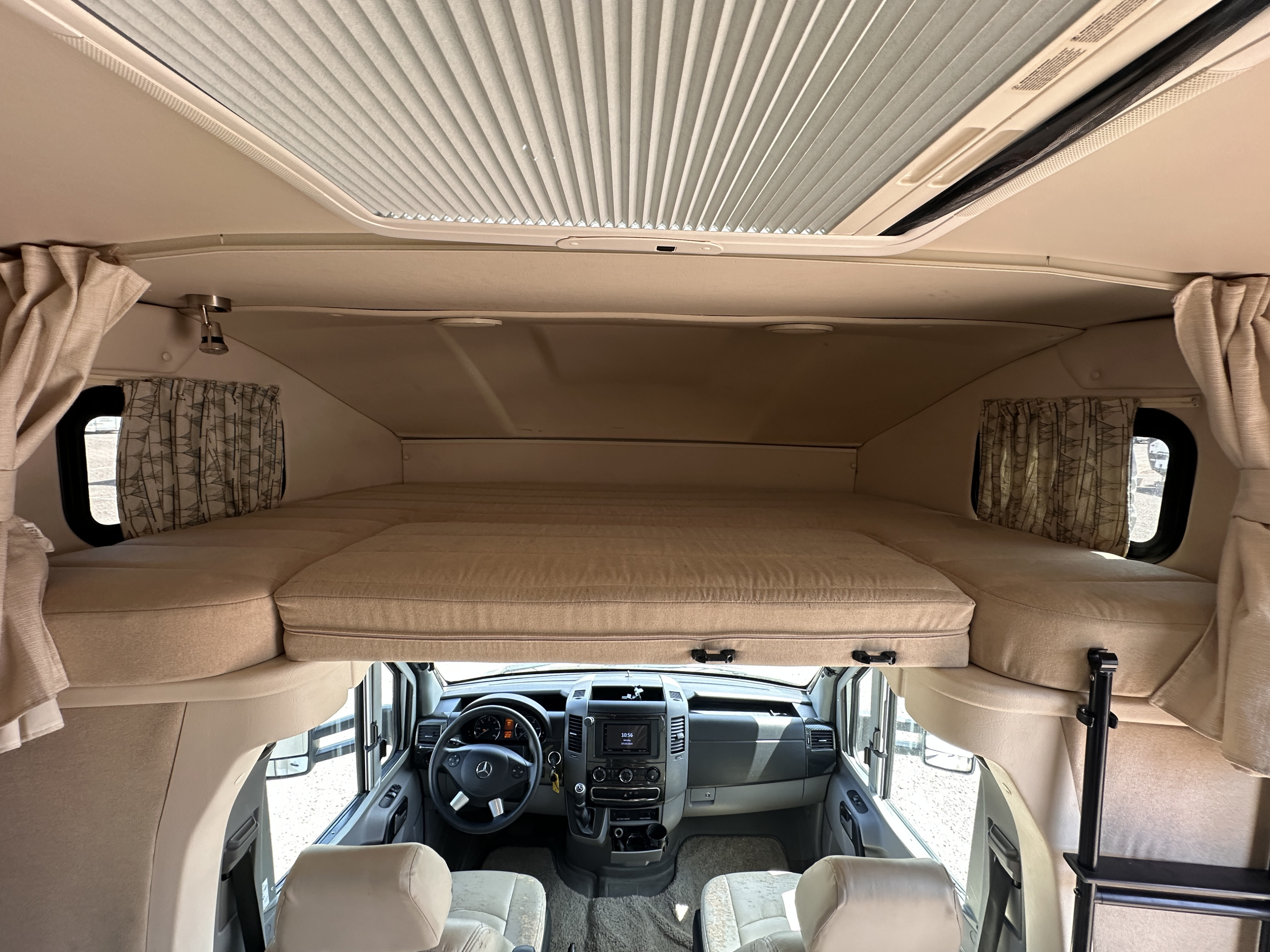 Front interior of an RV rental with elevated cab-over bed, large pleated skylight, and driver's cockpit view with dashboard.. Winnebago View 2016