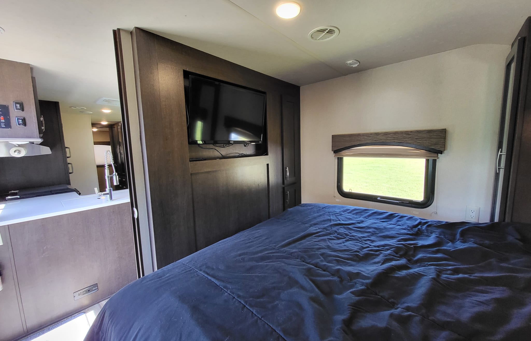RV rental interior: cozy bedroom with blue bedding, TV, and a glimpse into the kitchen area. Your comfortable home on wheels.. Forest River EVO T3250 2018