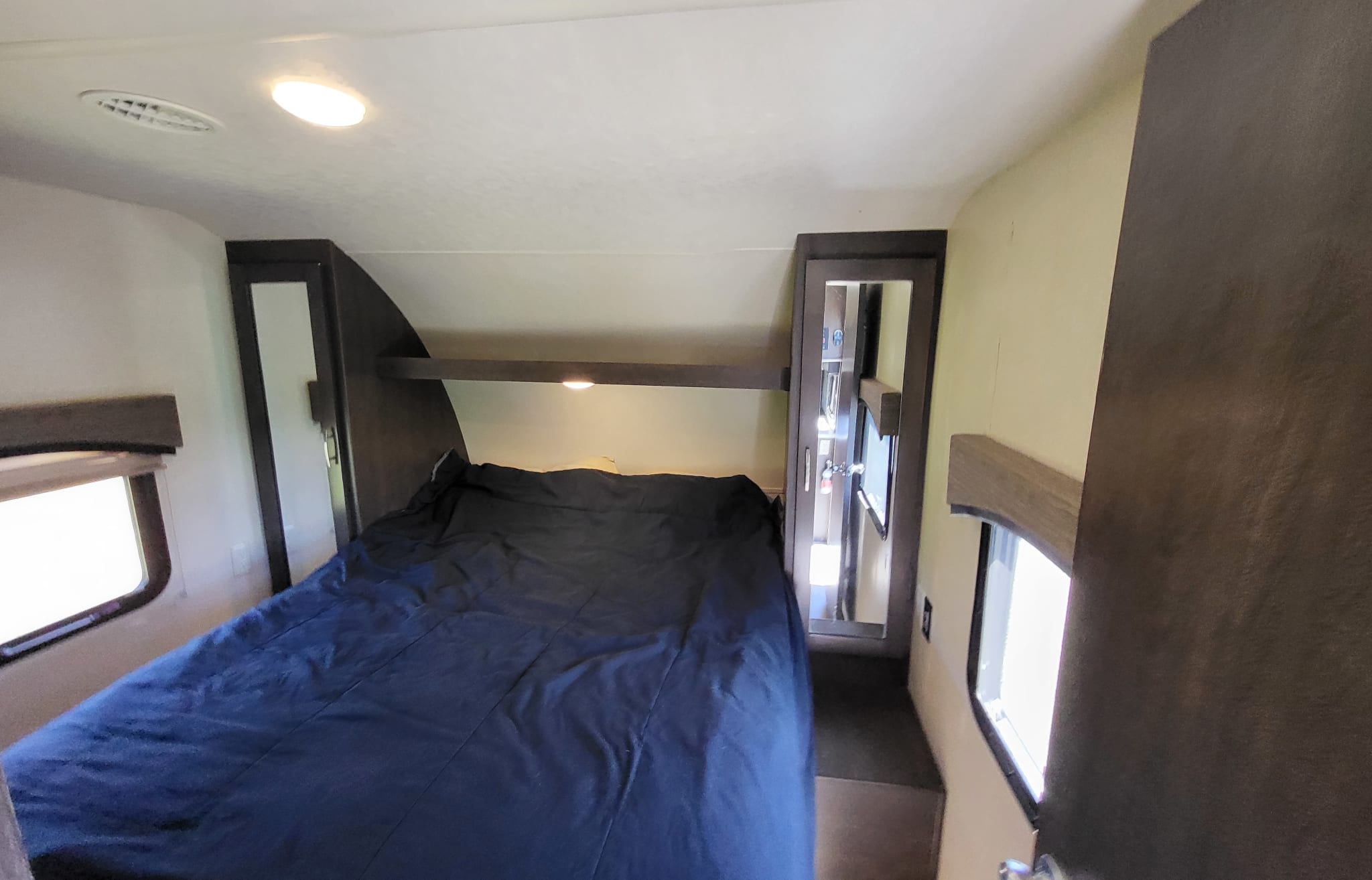 An RV rental's compact bedroom: blue bed, side windows, built-in storage, and overhead lights for comfort.. Forest River EVO T3250 2018