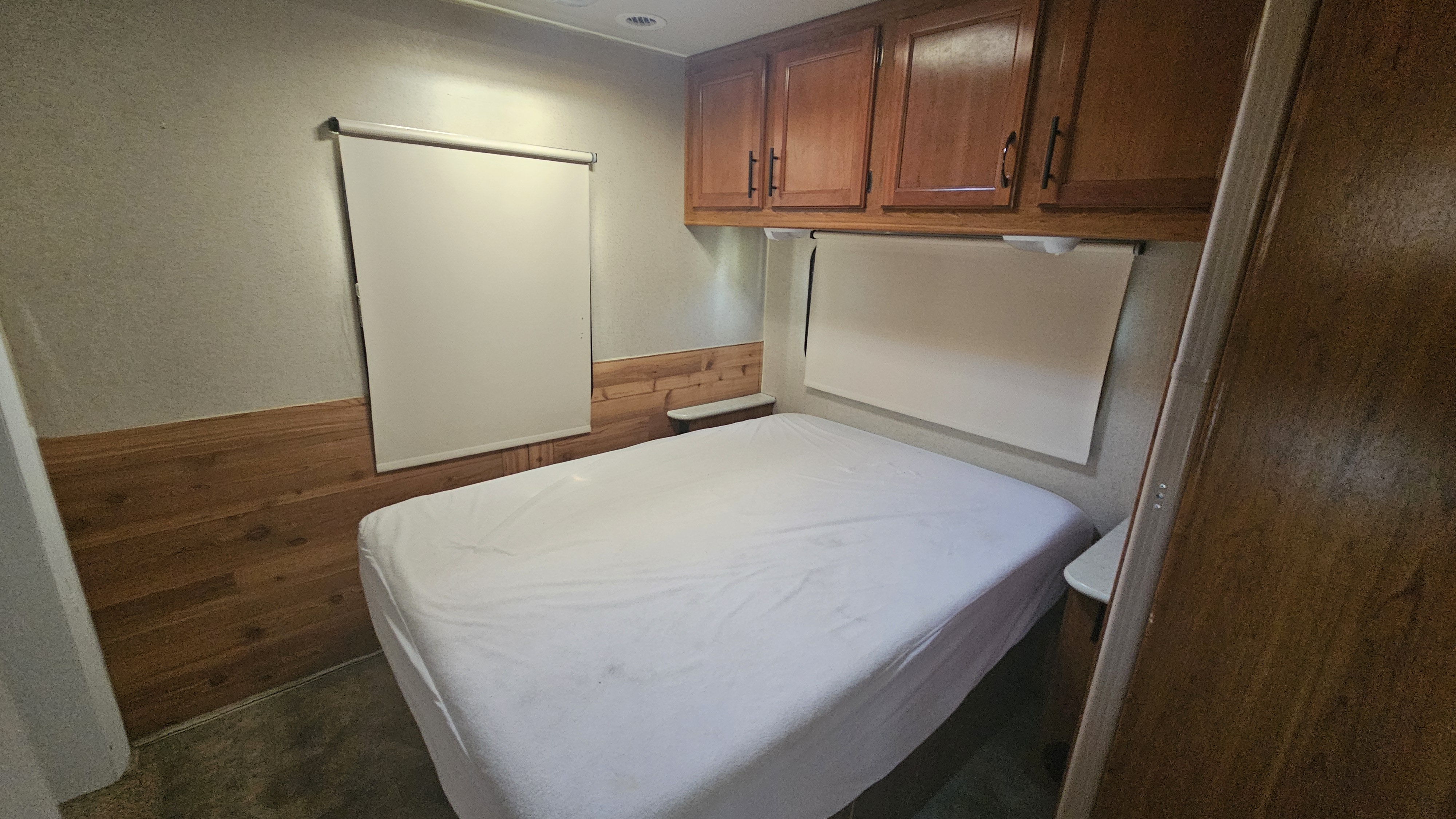 RV rental bedroom: cozy bed with white sheets, overhead cabinets, and wood paneling for a comfortable stay.. Jayco Redhawk 2016