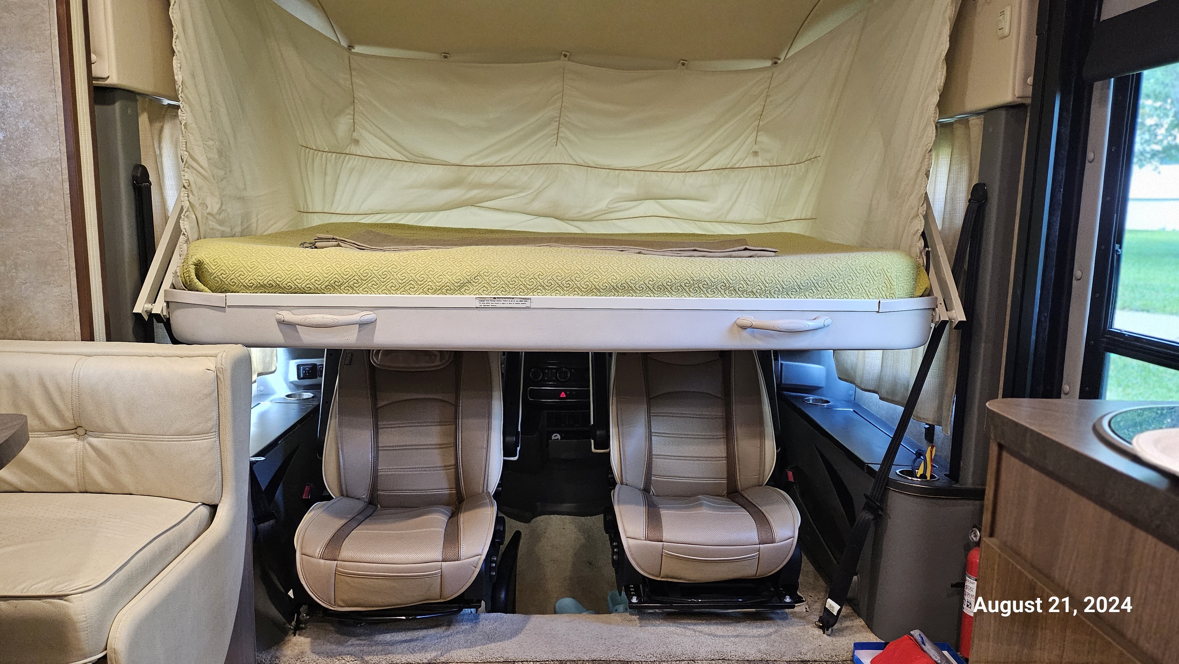 RV rental interior: A large pull-down bed with green quilt is lowered over the front captain's chairs, optimizing space for travel.. Winnebago Via 2014
