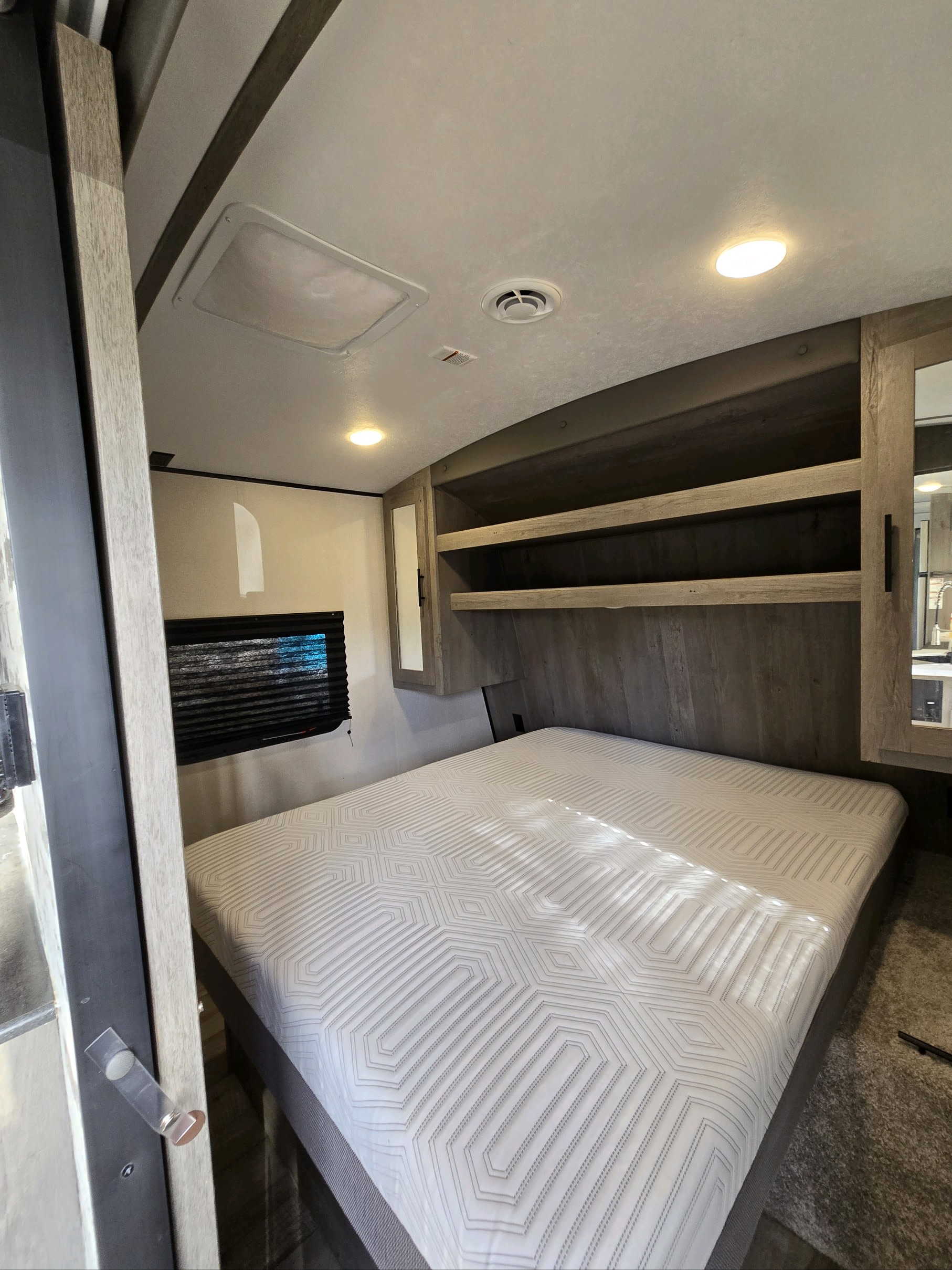 Cozy RV rental bedroom featuring a patterned bed, built-in shelves, bright lighting, and a window for comfortable living.. Keystone RV Springdale 2021