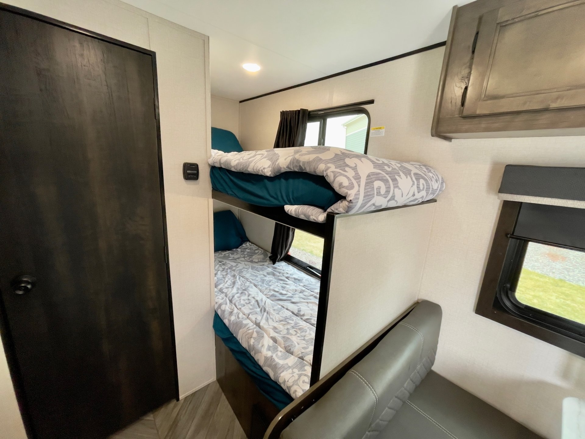 Inside an RV rental: two bunk beds with teal bedding, a dark door, and a gray dinette area. Cozy and practical RV living.. Highland Ridge Olympia Sport 2022