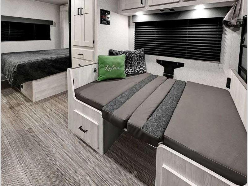 Modern RV rental interior featuring a comfortable bedroom and versatile dinette seating with grey cushions, ready for your next adventure.. Entrada East to West 2024