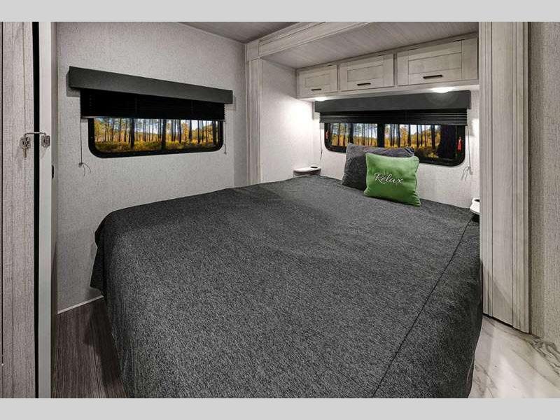 Comfortable RV rental bedroom featuring a cozy bed, overhead cabinets, and scenic nature views from the windows.. Entrada East to West 2024