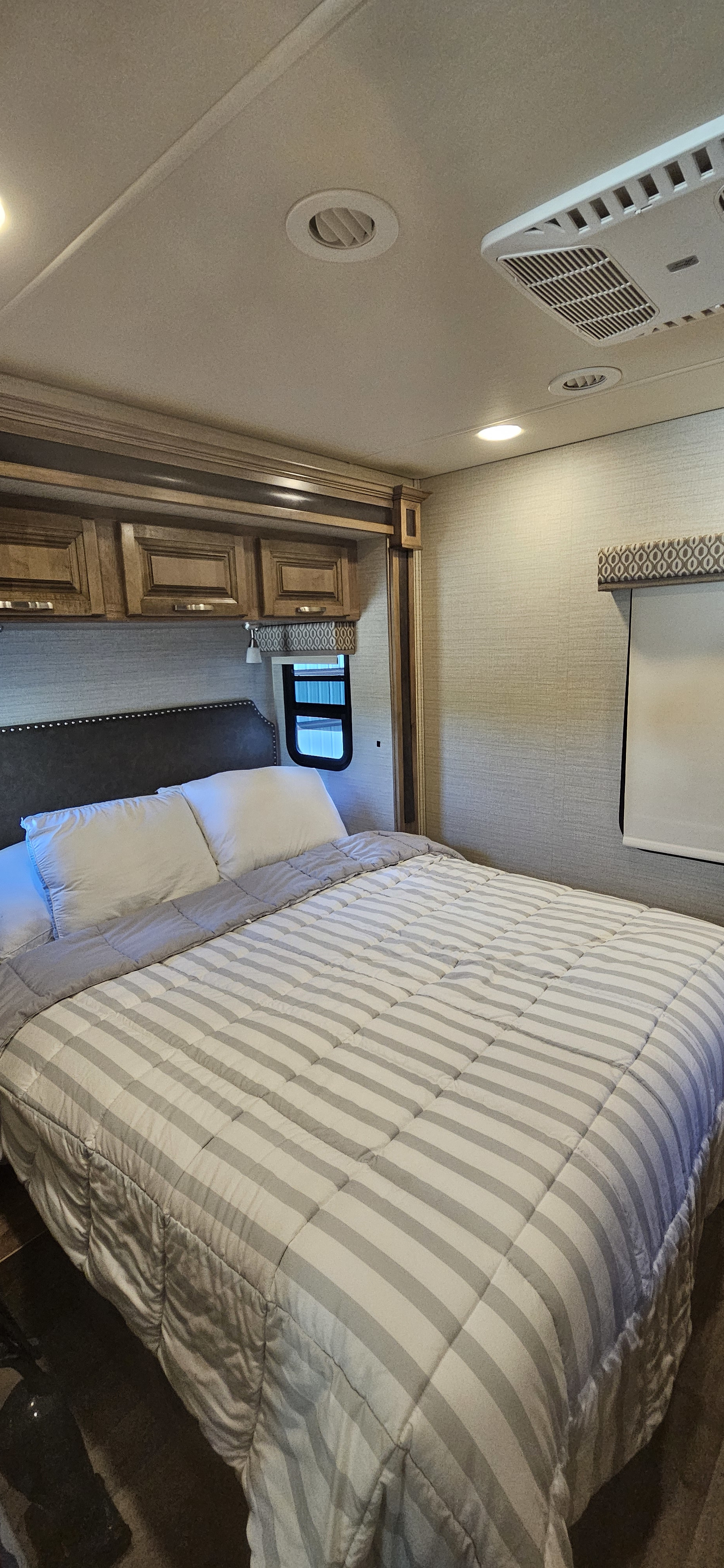 Cozy RV rental bedroom featuring a comfortable bed with a striped comforter, overhead storage, and AC unit.. Jayco Precept 2019