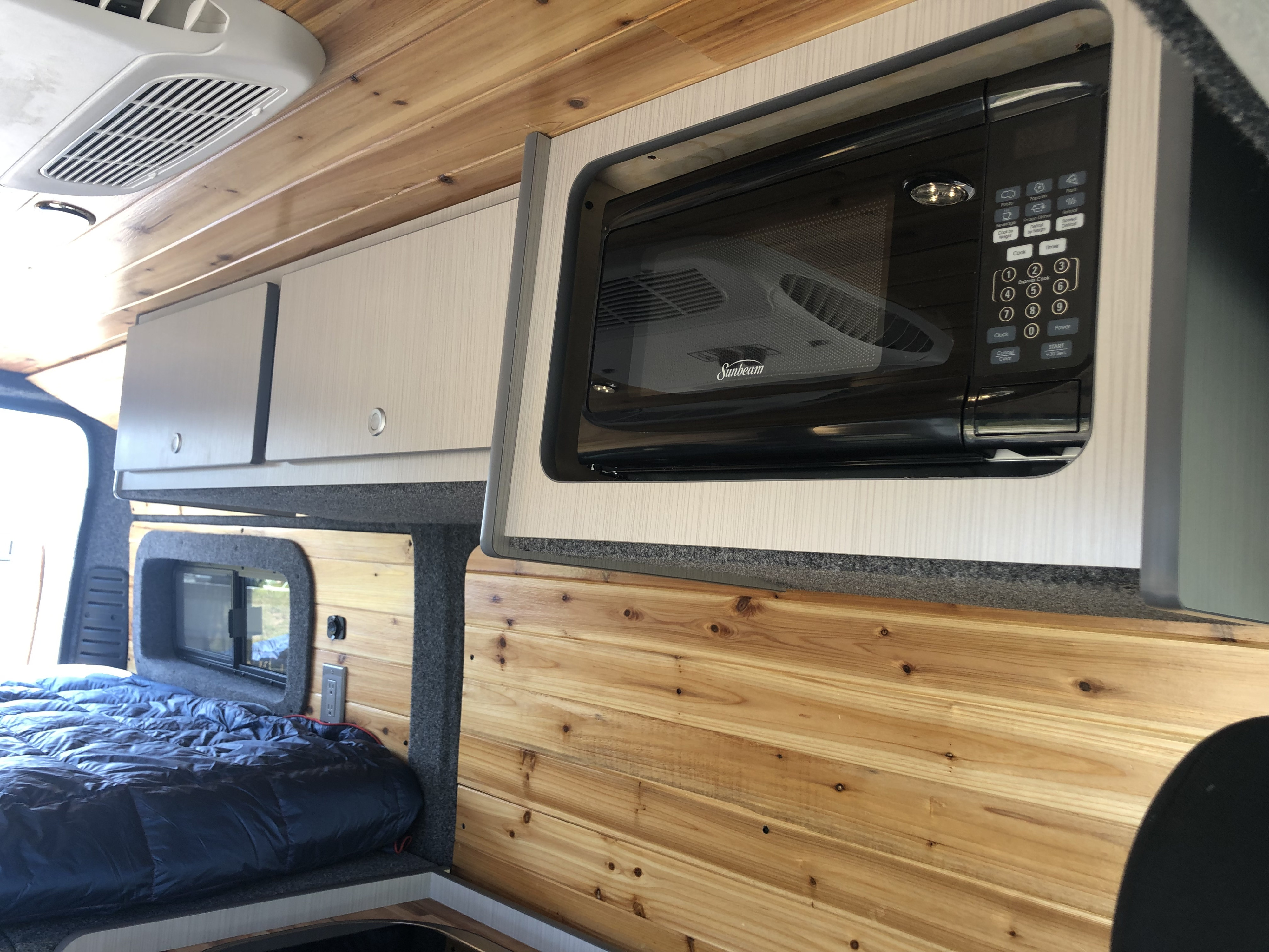 Well-equipped RV rental with a Sunbeam microwave, wood paneling, overhead cabinets, and a bed. Ideal for road trips.. Dodge Promaster- Alpine Edition OA7 2020