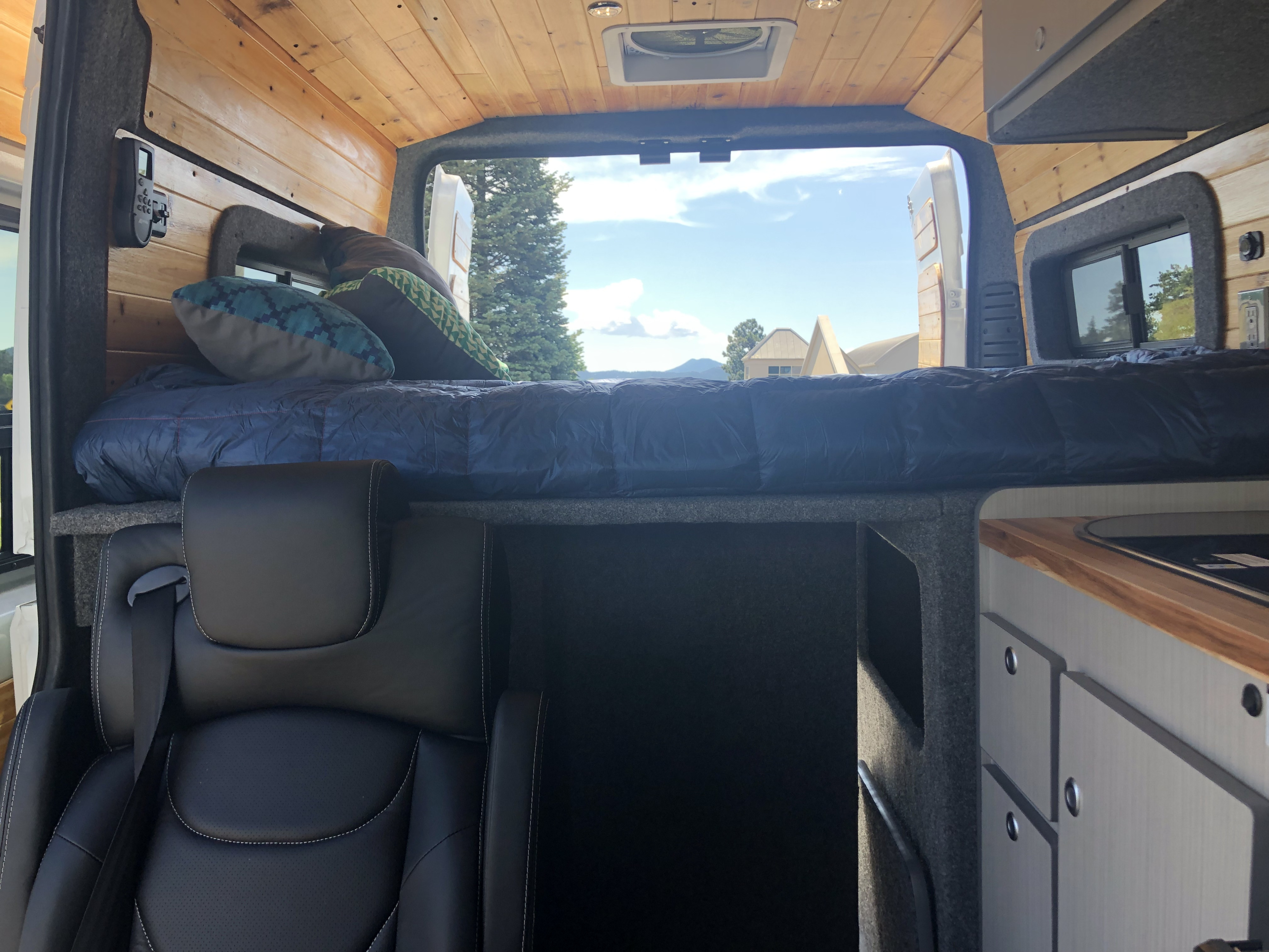 Customized RV rental interior with raised bed, black leather seat, wooden ceiling, and a compact kitchenette.. Dodge Promaster- Alpine Edition OA7 2020