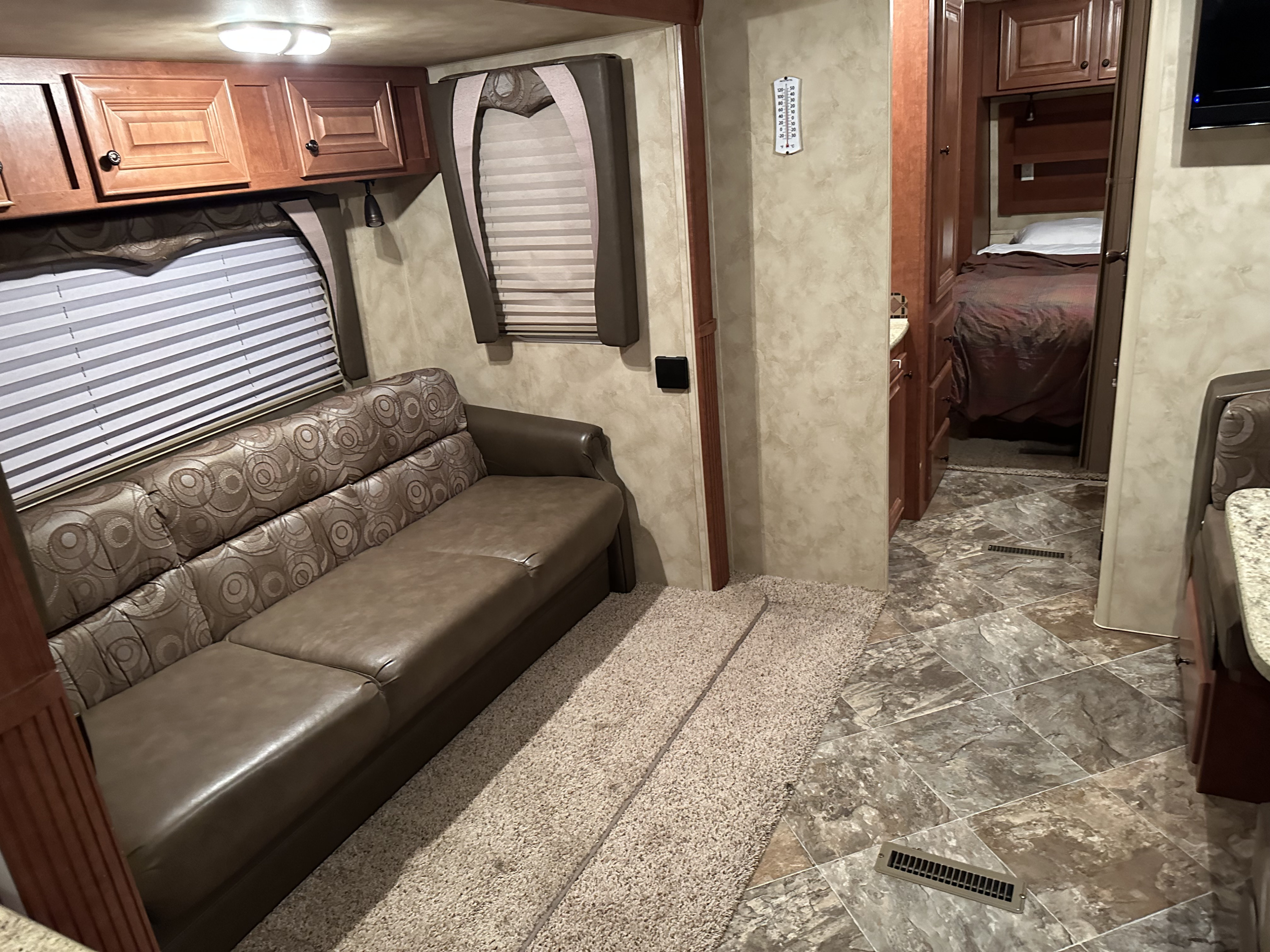 Inside this rv rental: a brown sofa, large window, and overhead cabinets in the living area, with a bedroom visible beyond.. Northwood Mfg Arctic Fox 2013