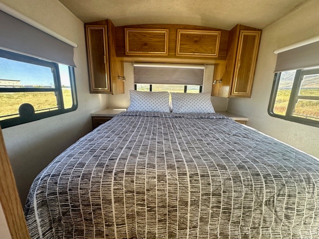 Cozy RV rental bedroom with a comfortable bed, patterned bedding, wooden cabinets, and scenic outdoor views through windows.. Flair-Fleetwood Flair-Fleetwood Motorhome 2002