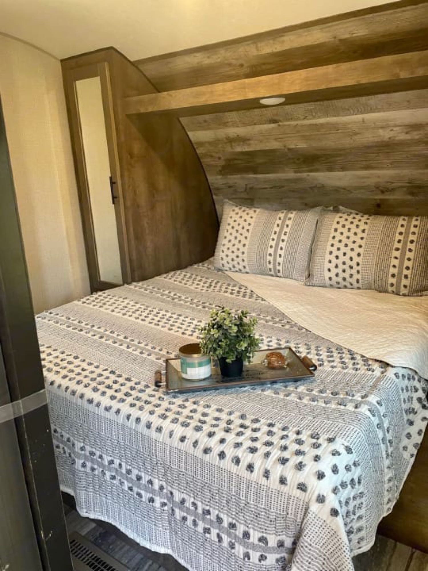 Cozy RV rental bedroom with patterned bedding, wood walls, and a tray holding a plant, candle & pastry.. KZ 4EZTL3322L7099109 2020
