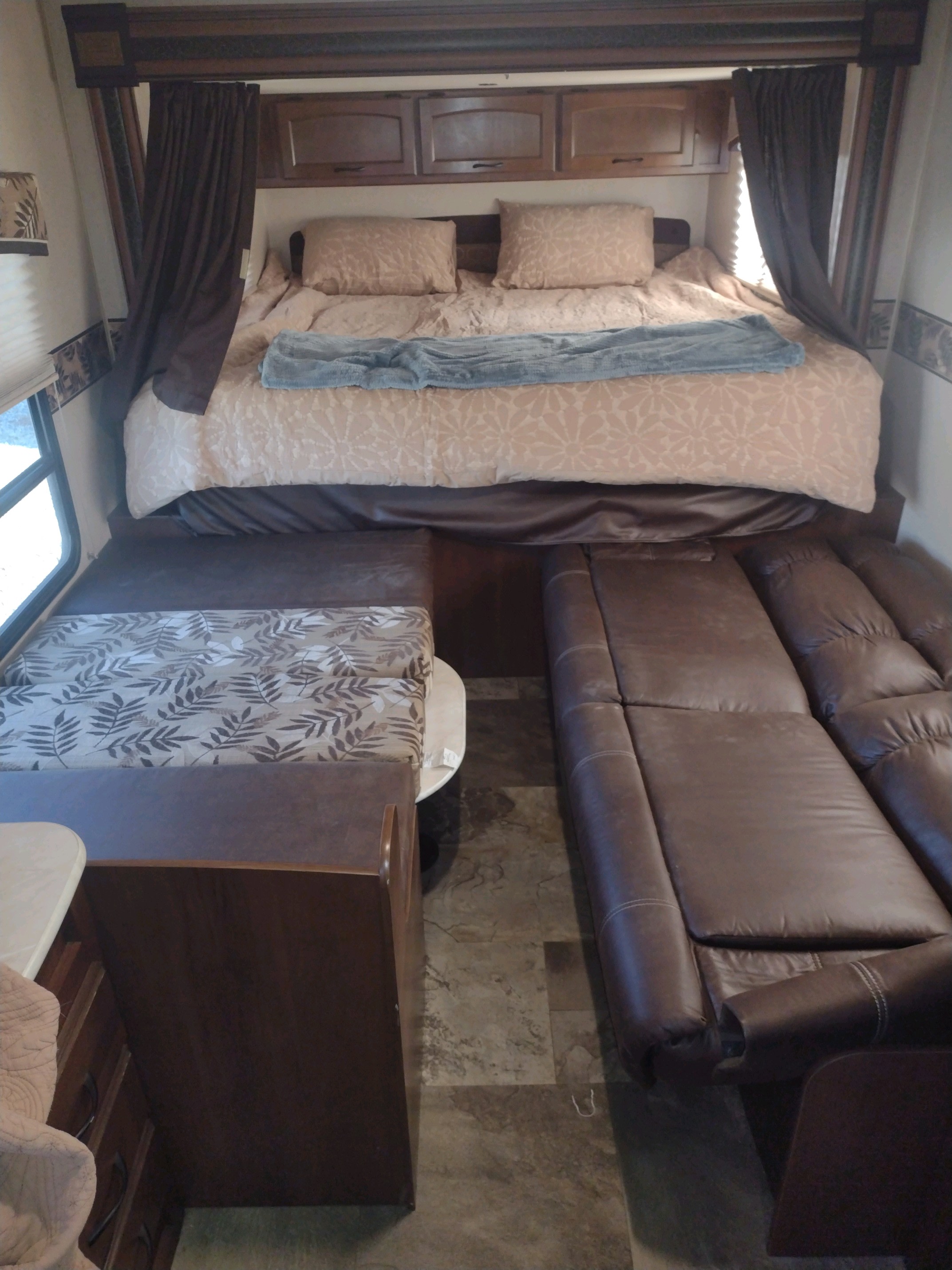 Cozy RV rental interior with a raised bed, patterned dinette, and a long leather sofa. Perfect for comfortable travel.. Jayco Jay Feather Ultra Lite 2015