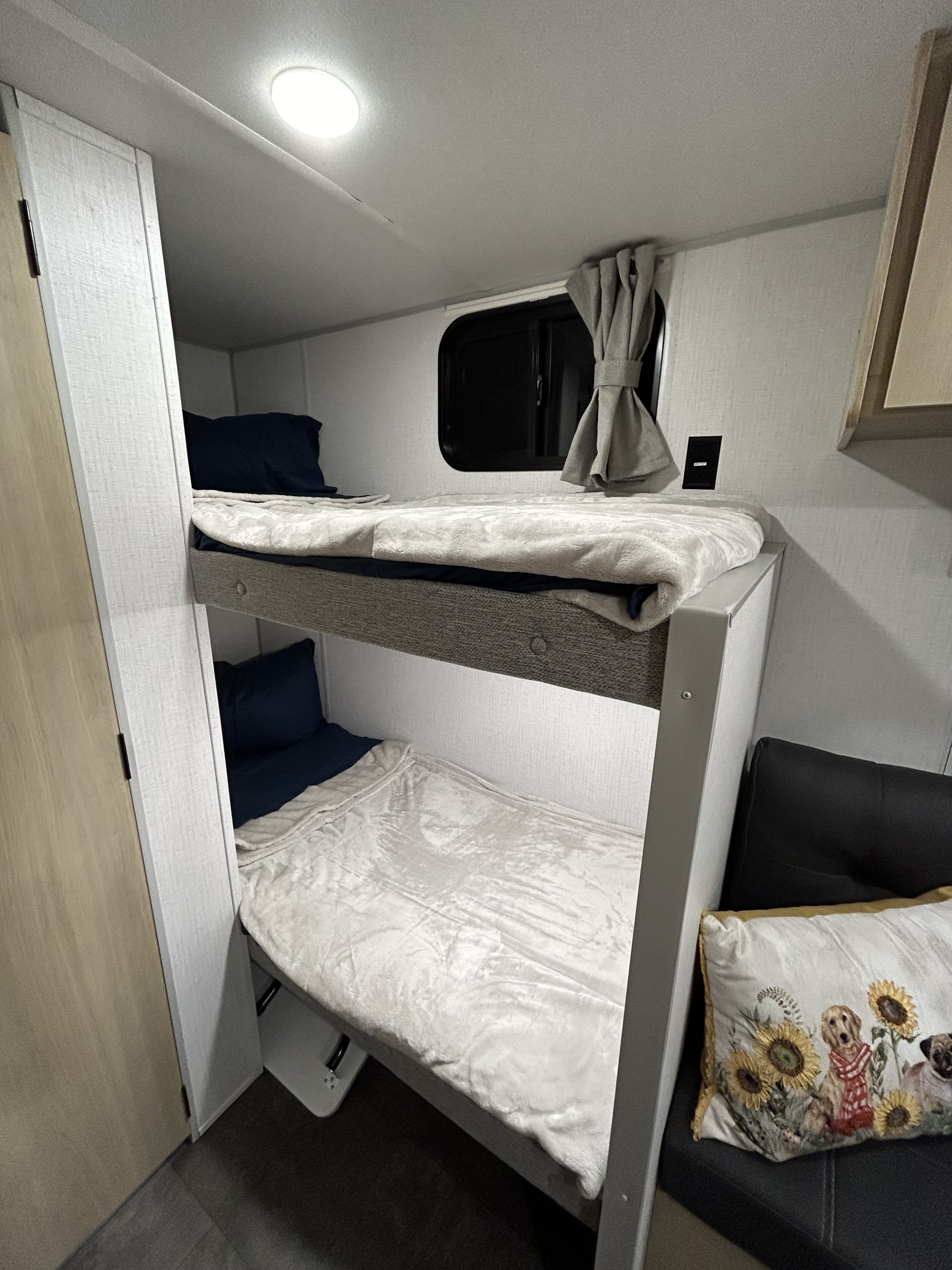 RV rental interior: Two cozy bunk beds with navy pillows & white blankets, window, and light. Compact sleeping space.. Wildwood 174BHLE 2025