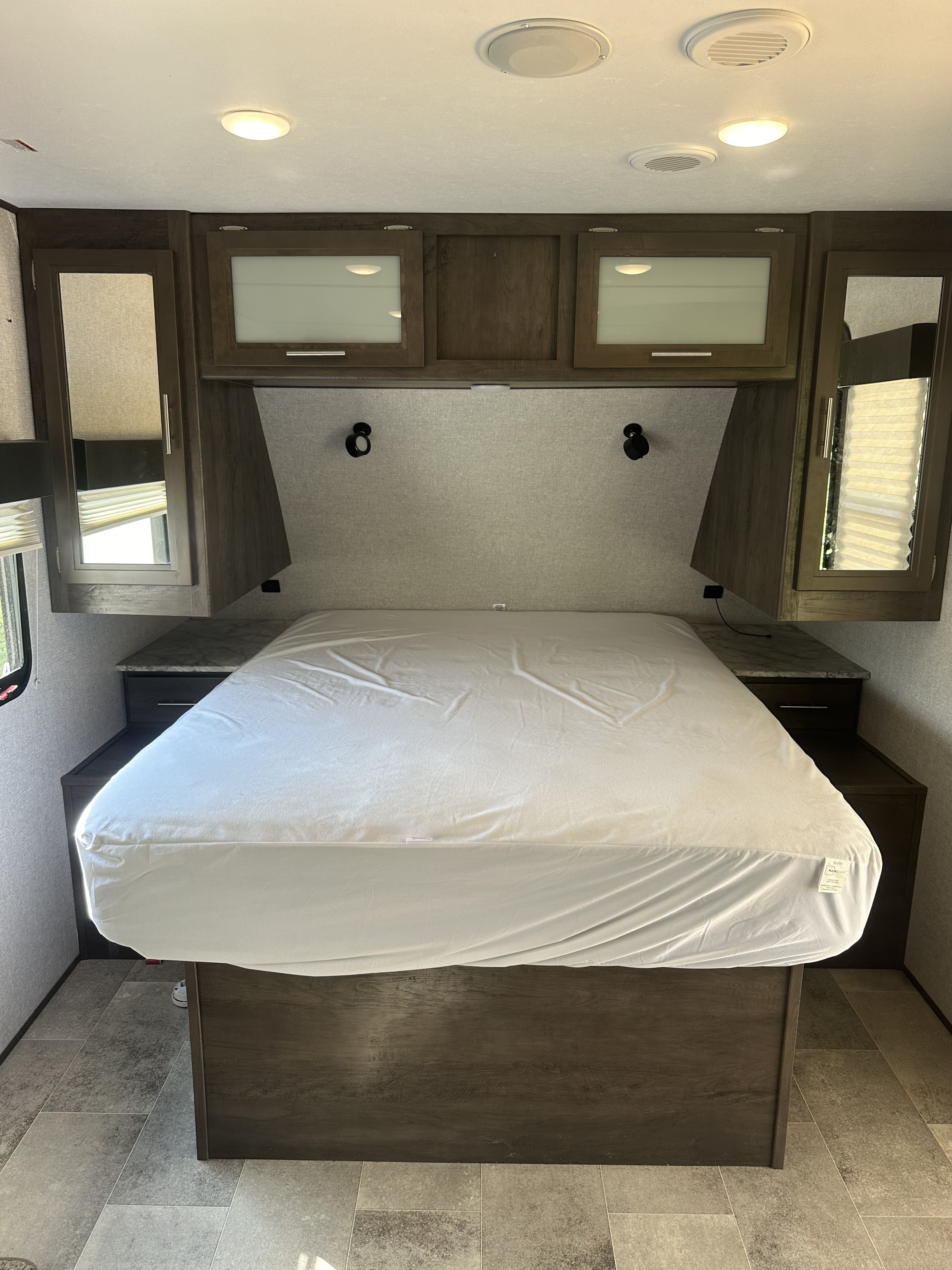 Clean RV rental bedroom ready for travel, featuring a queen bed, overhead storage, and modern interior lighting.. Dutchmen Coleman Light 2020