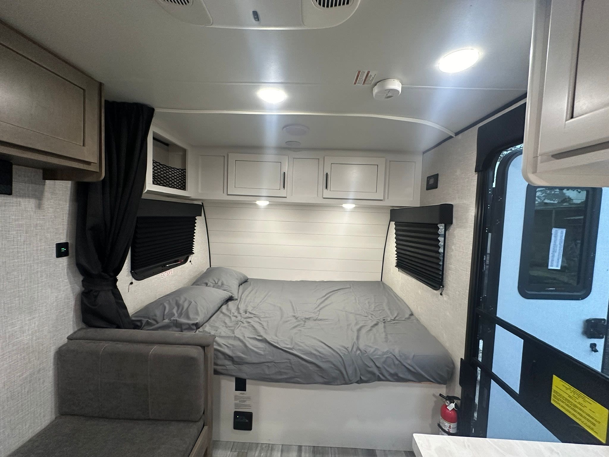 Bright RV rental bedroom with a cozy gray bed, storage cabinets, and a small seating area for your next adventure.. Jayco Jay Flight SLX 2024
